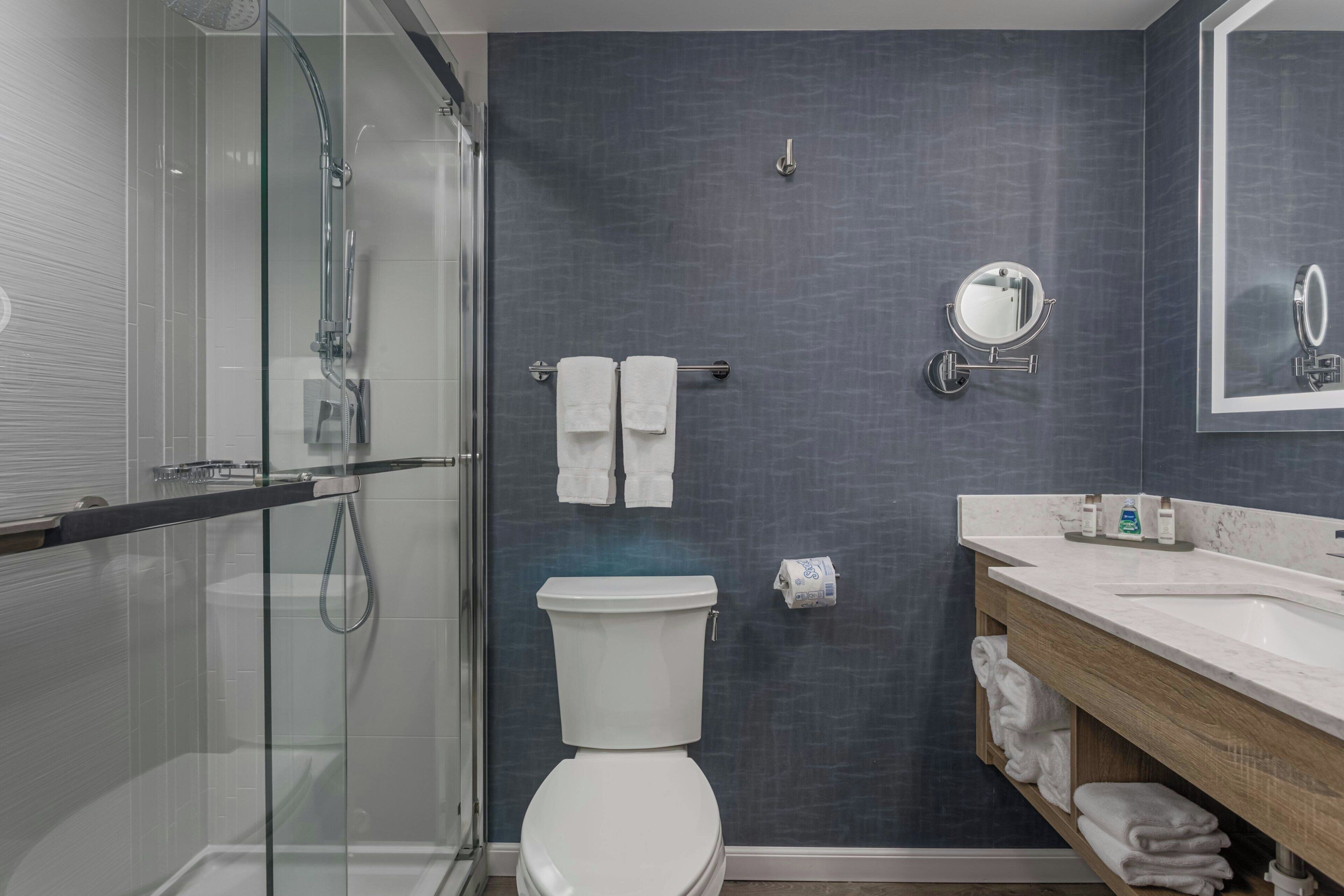 Un baño moderno con cabina de ducha de vidrio, inodoro blanco y tocador con espejo y lavabo.