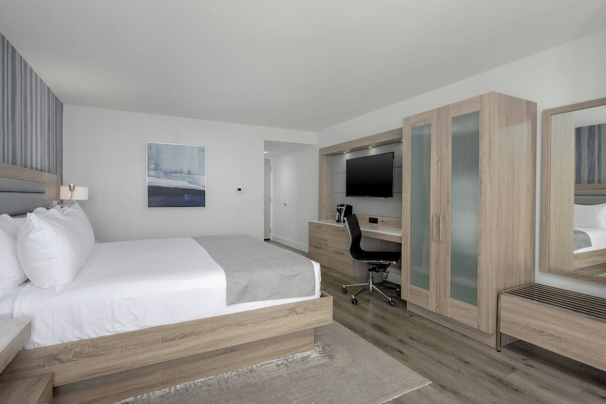 A modern hotel room with a bed, desk, TV, and wardrobe.