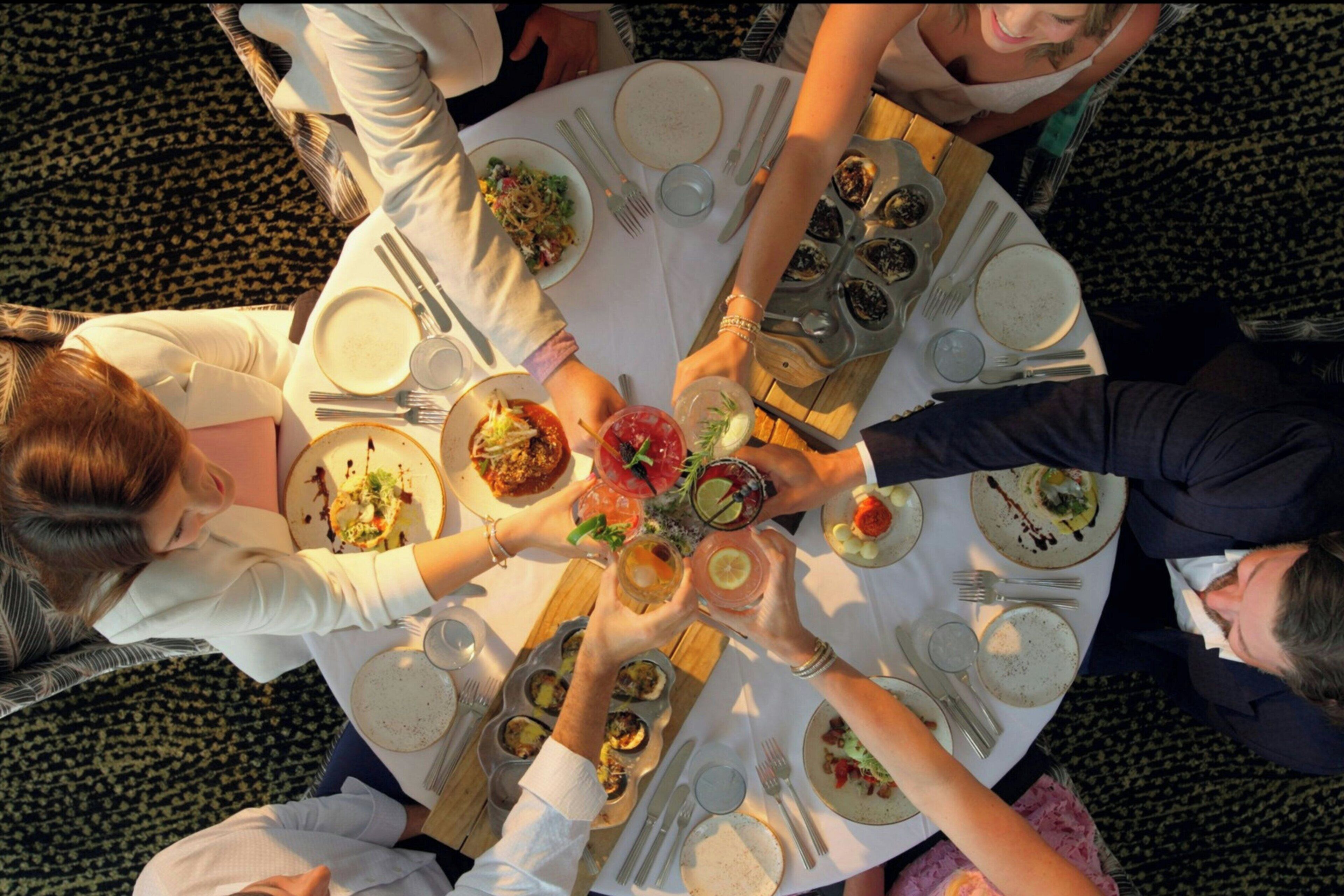 A group of people seated around a round table with various dishes and drinks, suggesting a social dining setting.