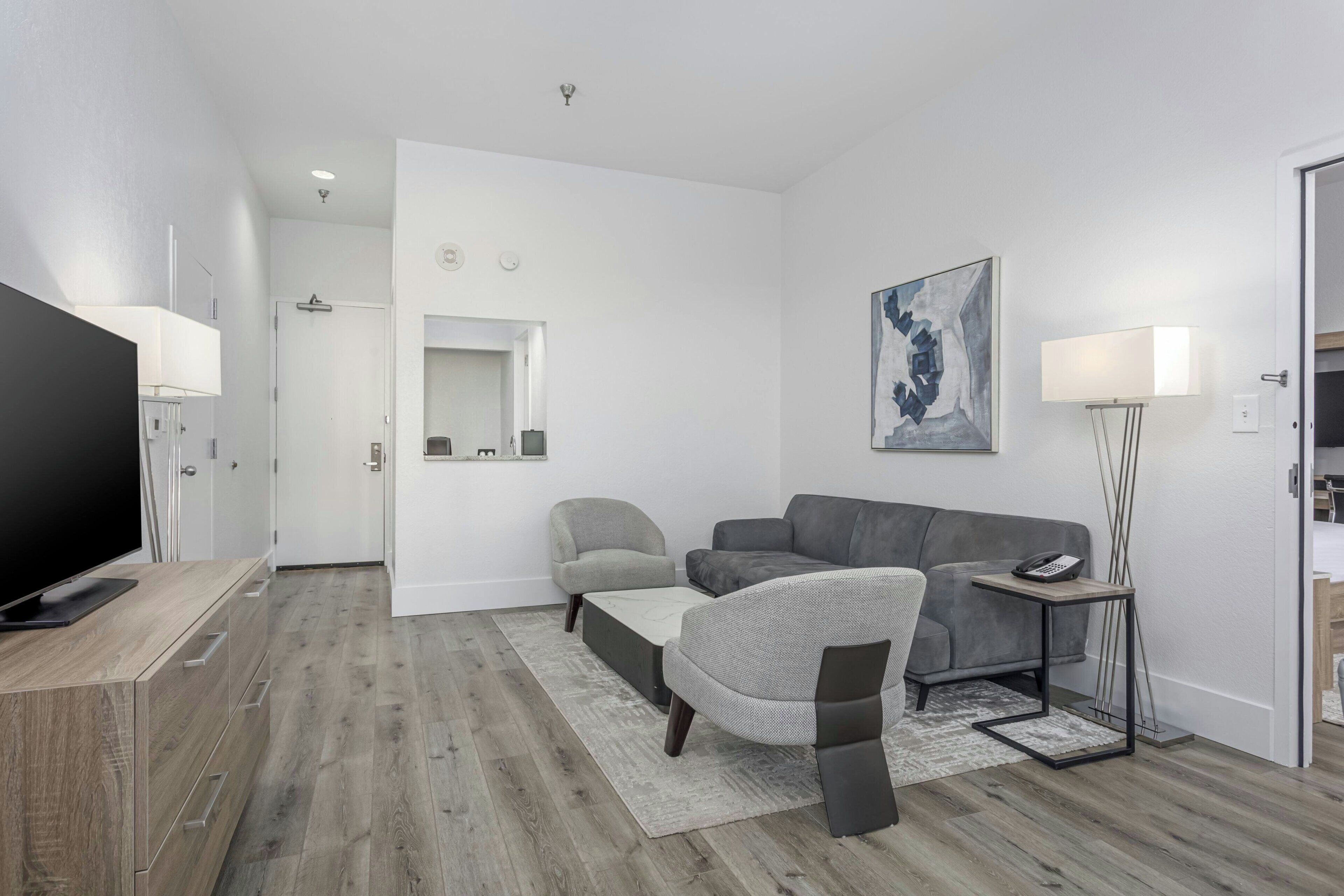 A modern living room with a flat-screen TV, grey sofas, a coffee table, a floor lamp, and a painting on the wall.