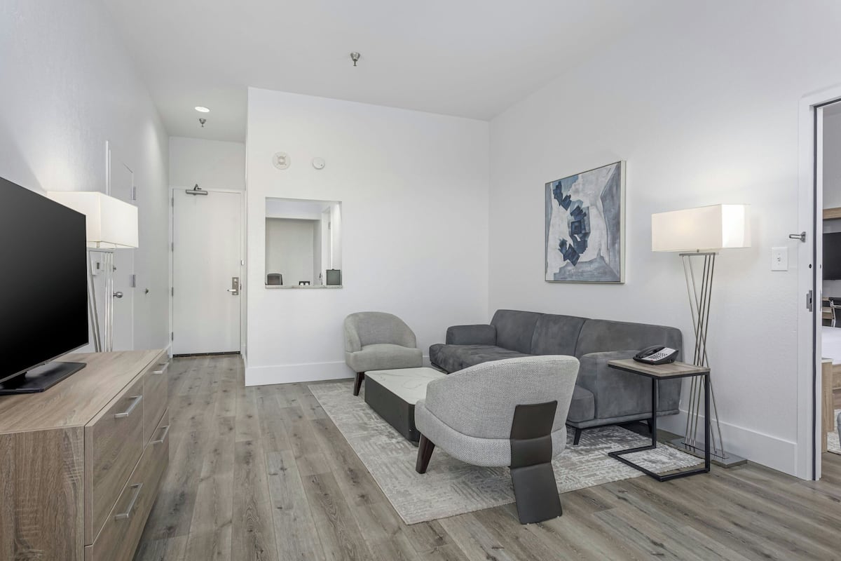 A modern living room with a flat-screen TV, grey sofas, a coffee table, a floor lamp, and a painting on the wall.