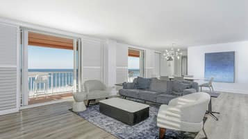 Ein modernes Wohnzimmer mit grauem Sofa, weißen Sesseln, einem Couchtisch und Blick auf das Meer durch große Fenster.