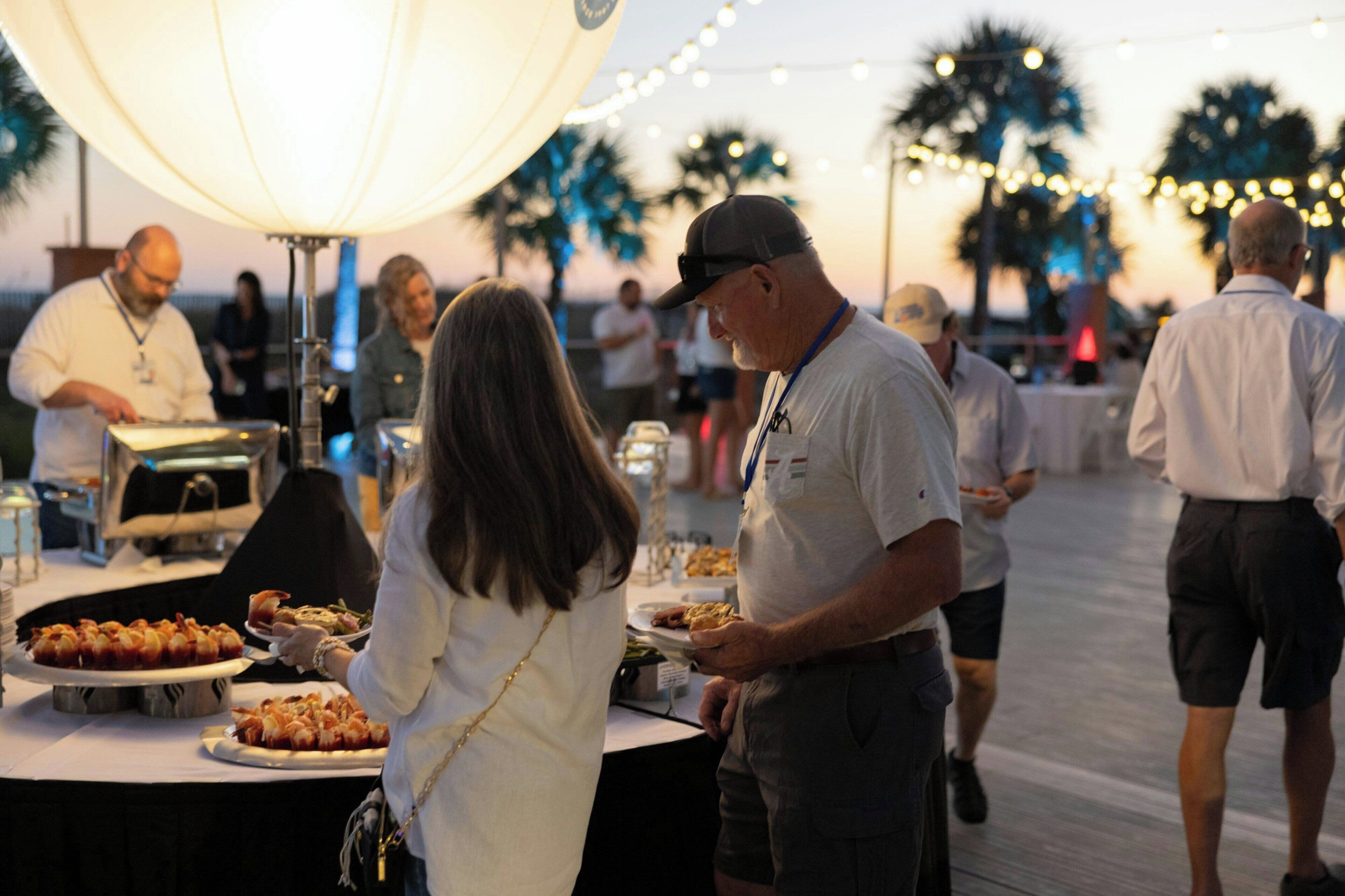 A group of people dining outdoors at a buffet with a table and food items.
