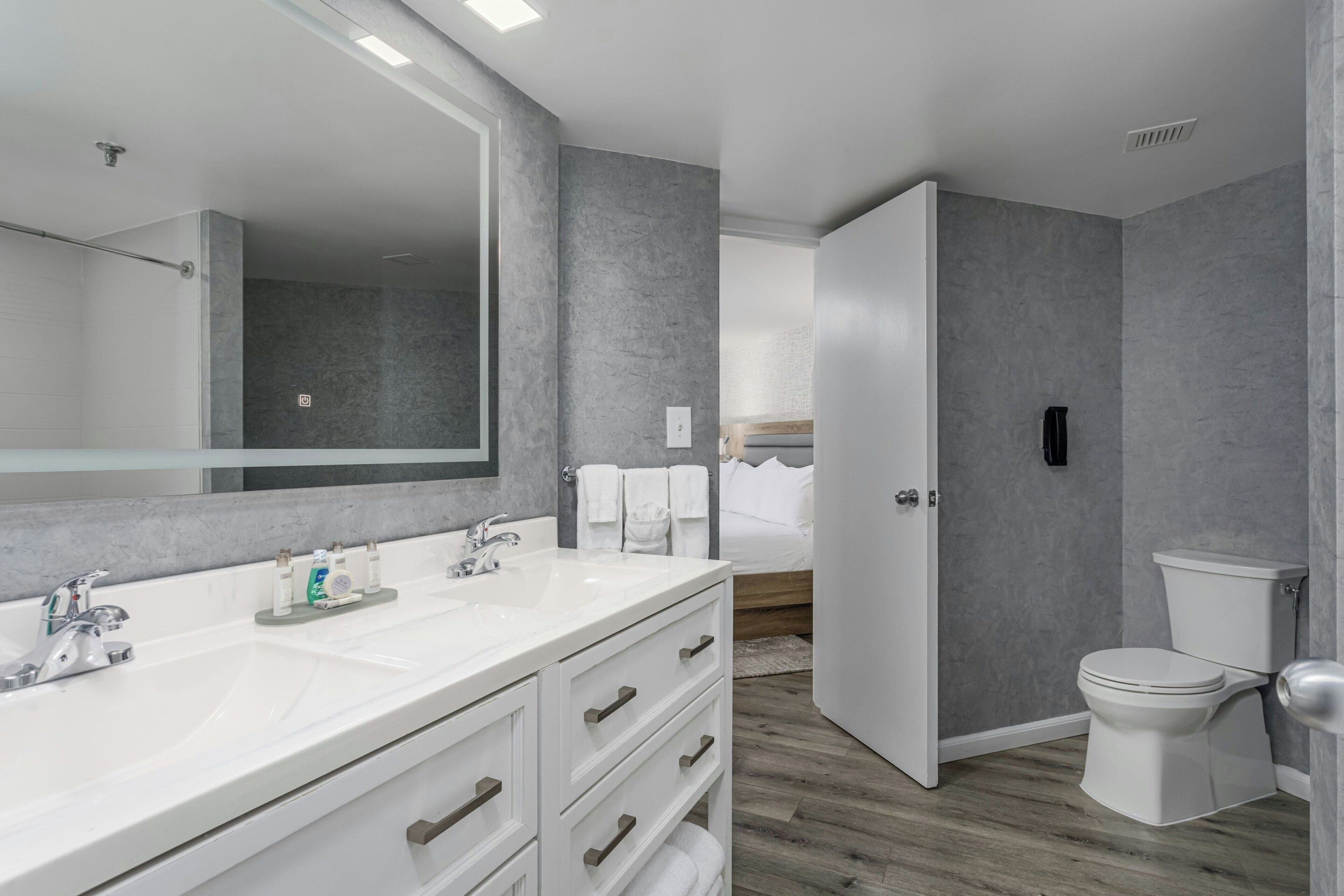 A modern bathroom with a large mirror, dual sinks, and a toilet.