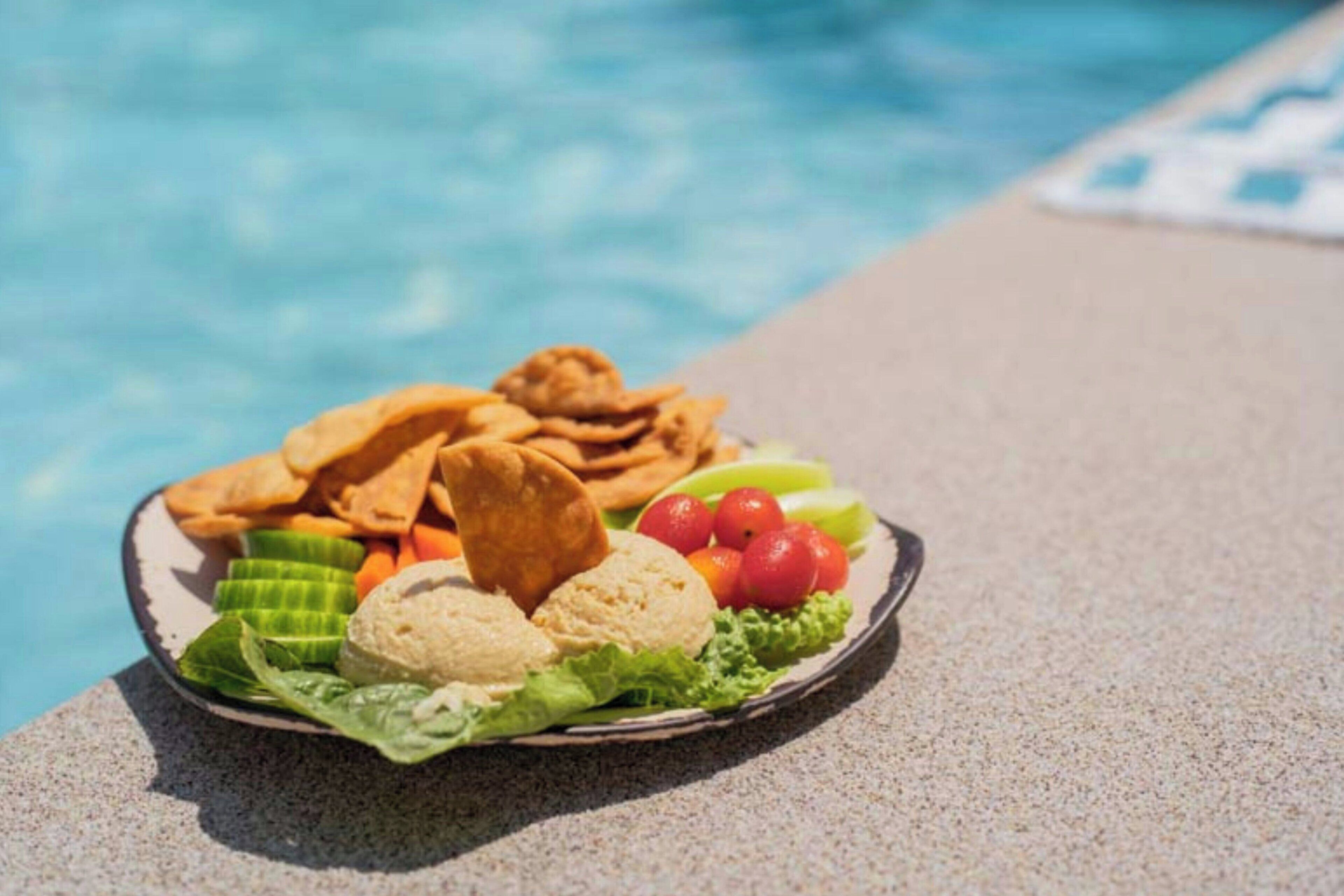 A plate of food by a poolside with a clear view of the water.