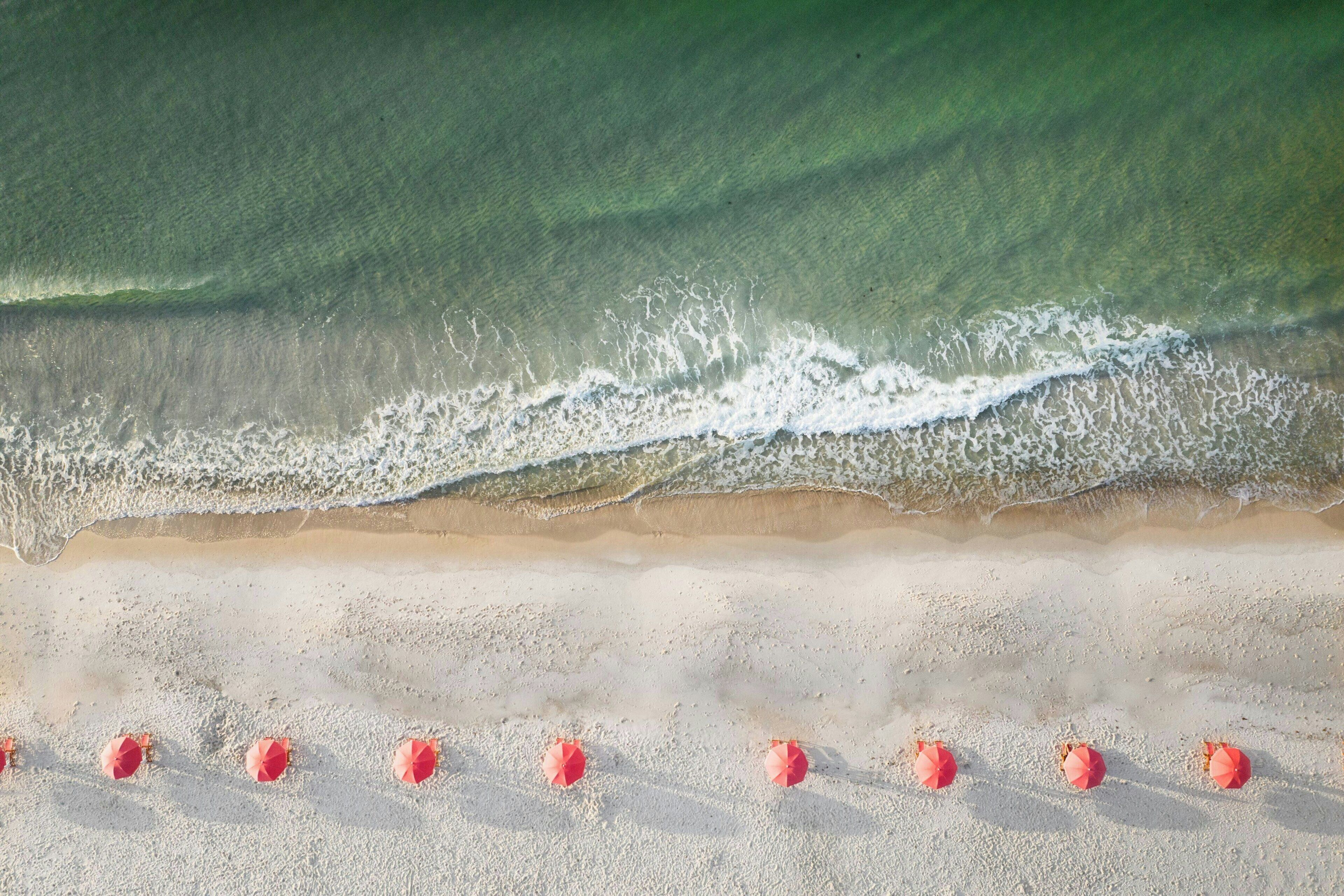 A beach with waves approaching the shore, and several red umbrellas lined up on the sand.