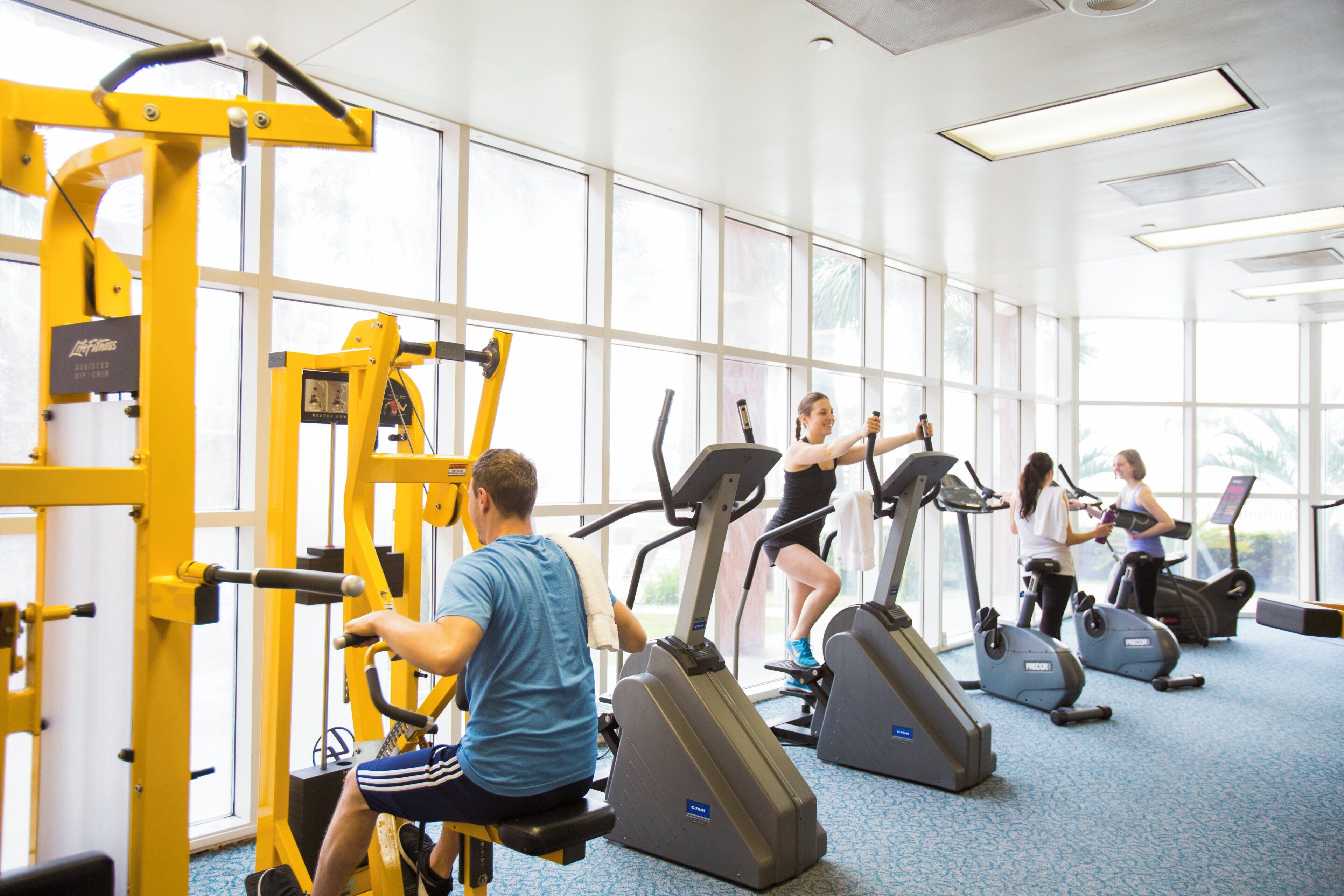 A gym with exercise equipment, large windows, and a blue carpet.