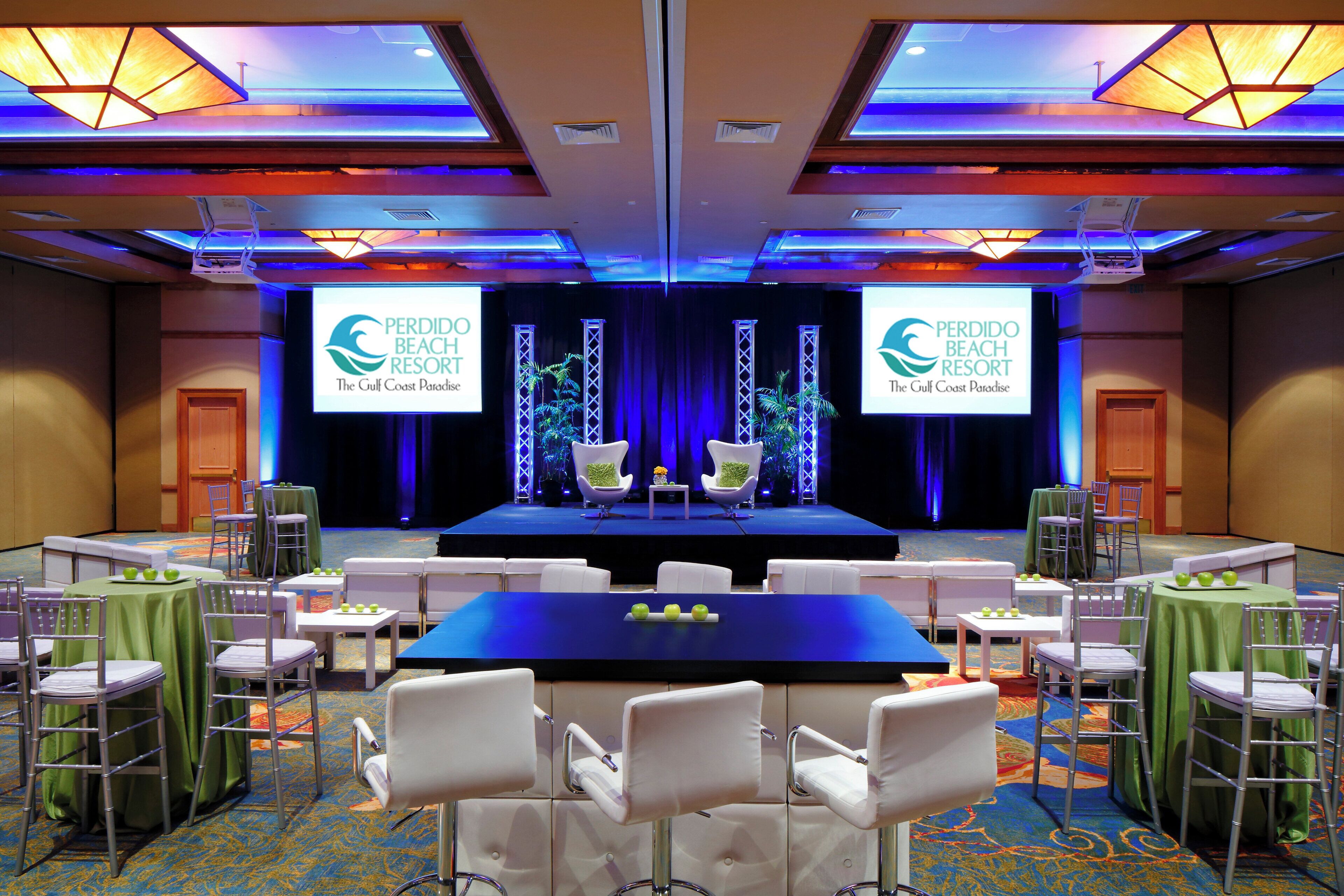 A conference room with a stage, tables, chairs, and a carpeted floor.