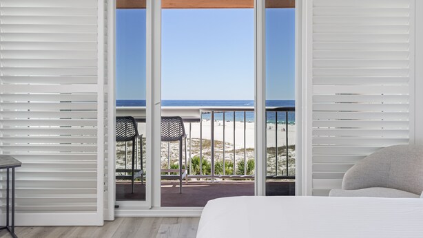 Una habitación con un amplio ventanal corredera que da a un balcón con vista a la playa y al océano.
