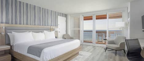 A modern hotel room with a large bed, a desk, a chair, and a balcony with a view.