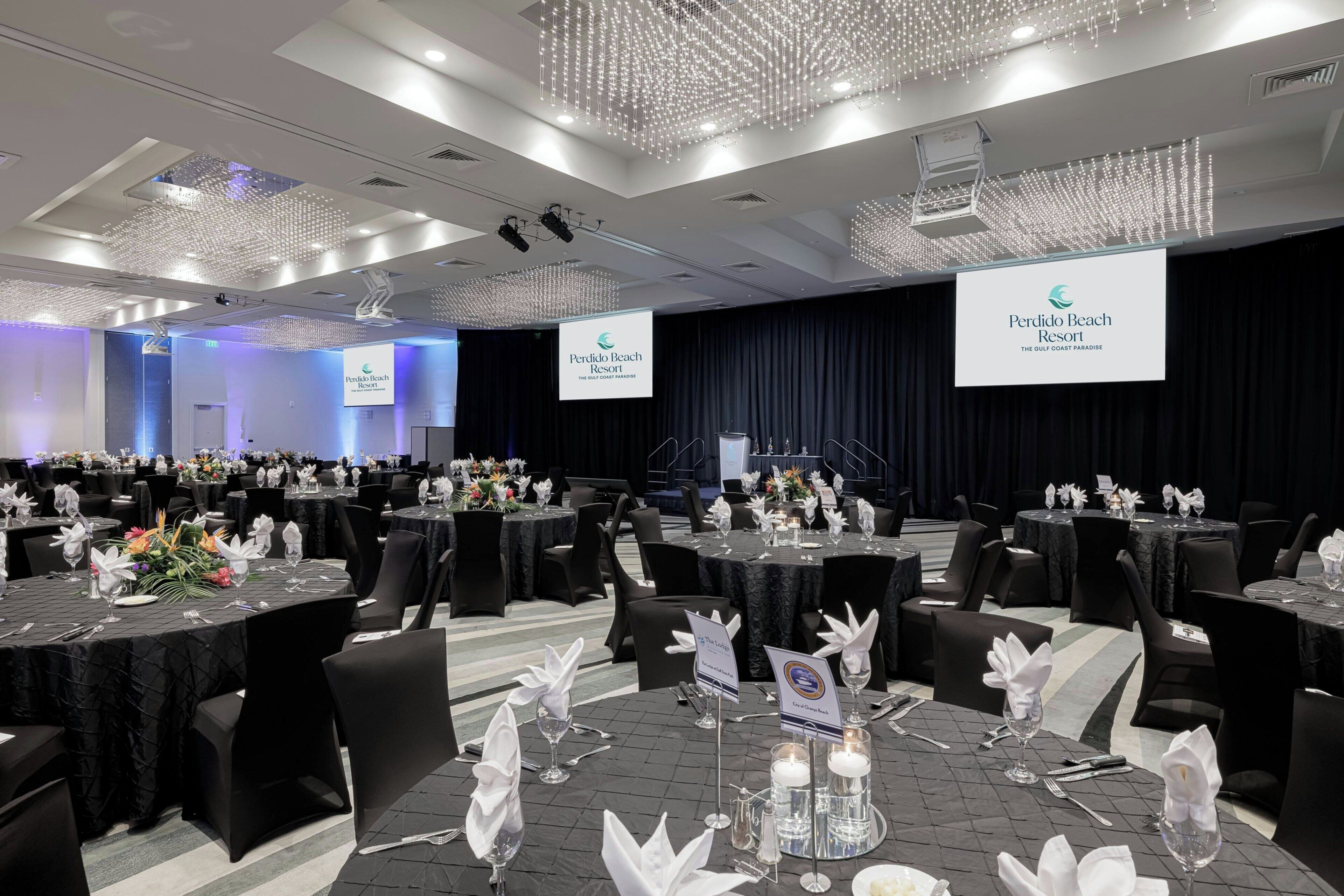 A banquet hall at Perdido Beach Resort with tables set for a formal event, featuring black tablecloths, white napkins, and floral centerpieces.