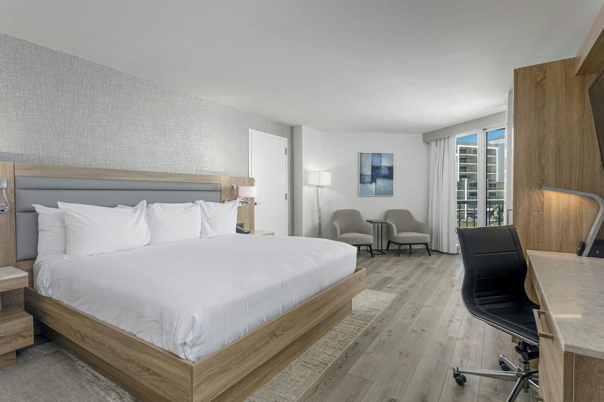 A hotel room with a large bed, a desk, a chair, and a view of the city through the window.