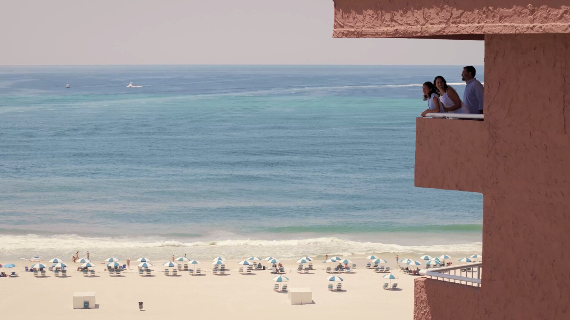 A beach view from a balcony with a clear ocean and a sandy beach with umbrellas.