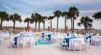 Espaço para eventos ao ar livre com mesas redondas e cadeiras brancas, montado para um evento formal.