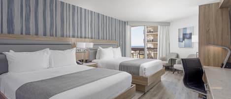 Hotellihuone, jossa on kaksi sänkyä, työpöytä, tuoli ja näkymä merelle.