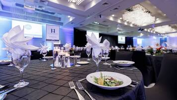 Una mesa de banquete dispuesta con servilletas blancas, copas de vino y platos de comida, con un candelabro colgando sobre ella.