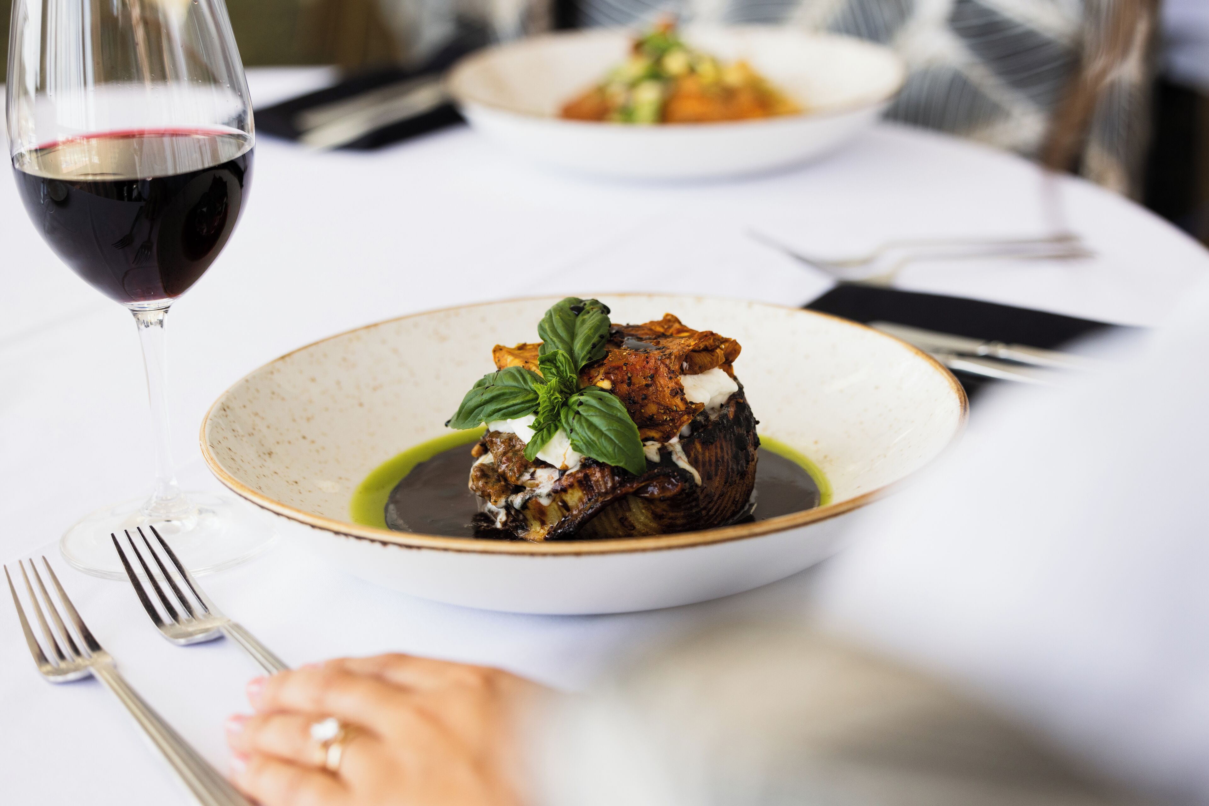 A dining table with a plate of food, a glass of red wine, and cutlery.