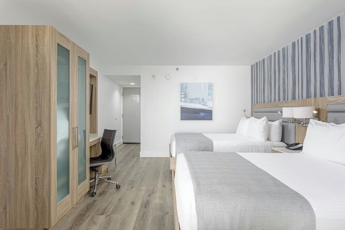 A hotel room with two beds, a desk, a chair, and a wardrobe with frosted glass doors.