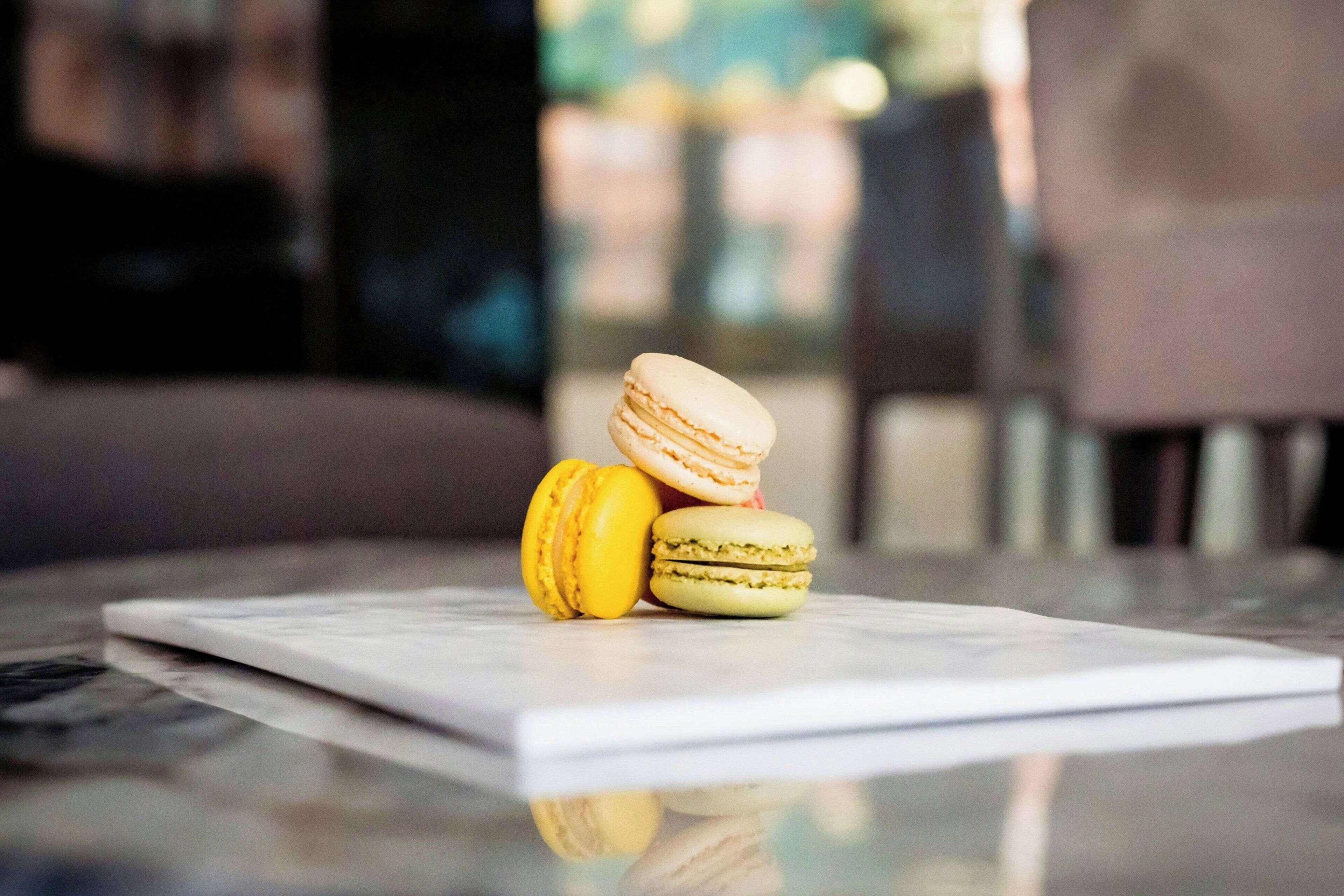 Three macarons on a white rectangular object, possibly a napkin, on a reflective surface.