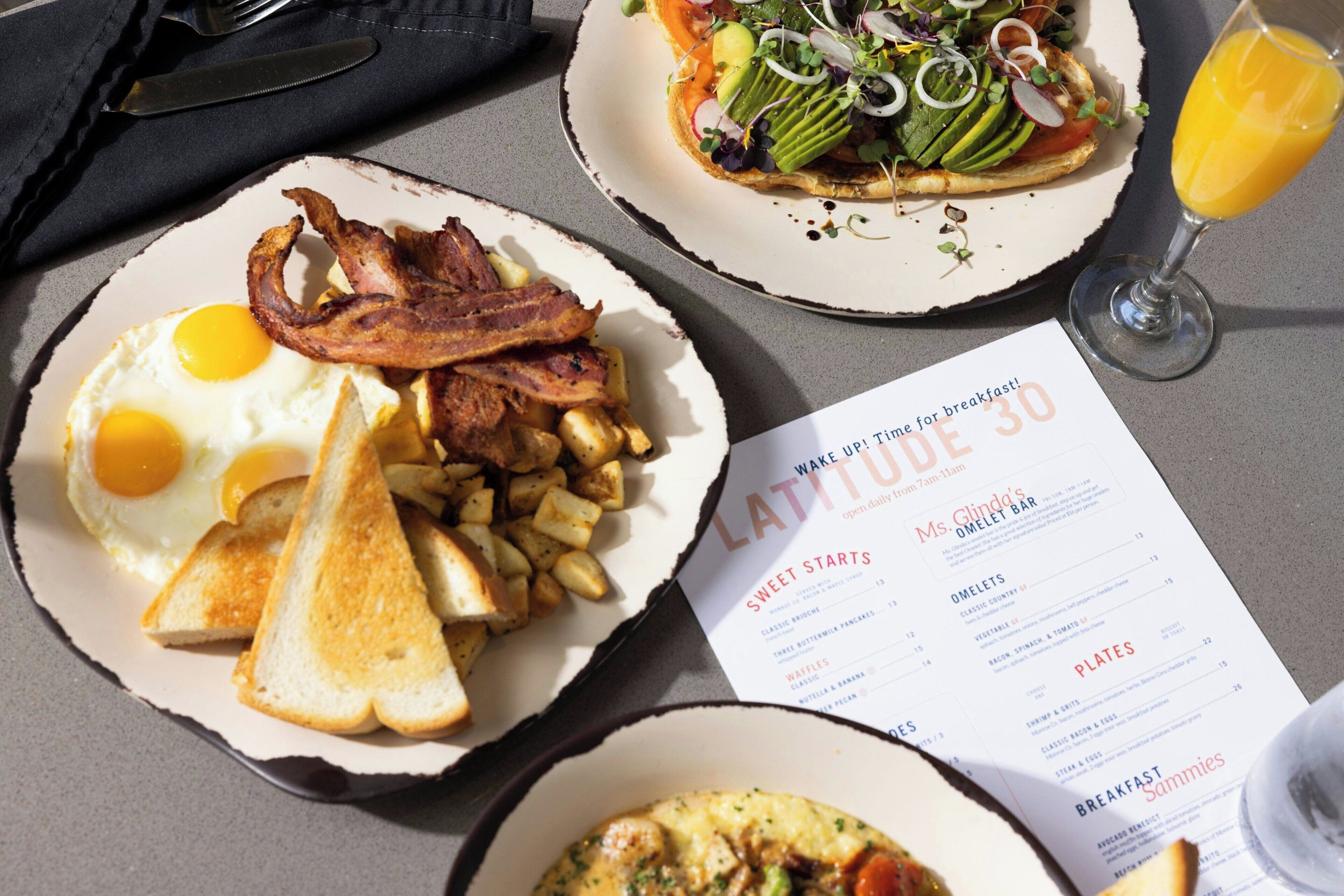 A breakfast setting with plates of food, a menu, and a glass of orange juice.