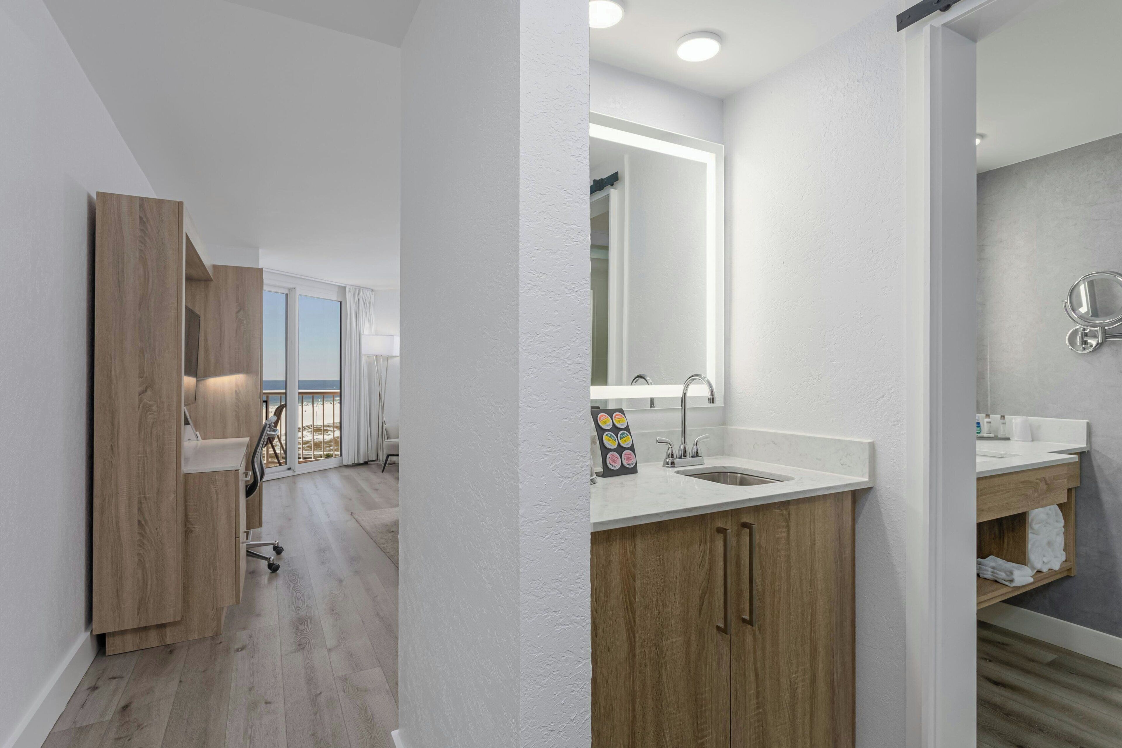 A modern bathroom with a large mirror, wooden cabinetry, and a white countertop.