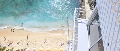 A beach with umbrellas and people, a staircase leading to a building, and a view of the ocean.