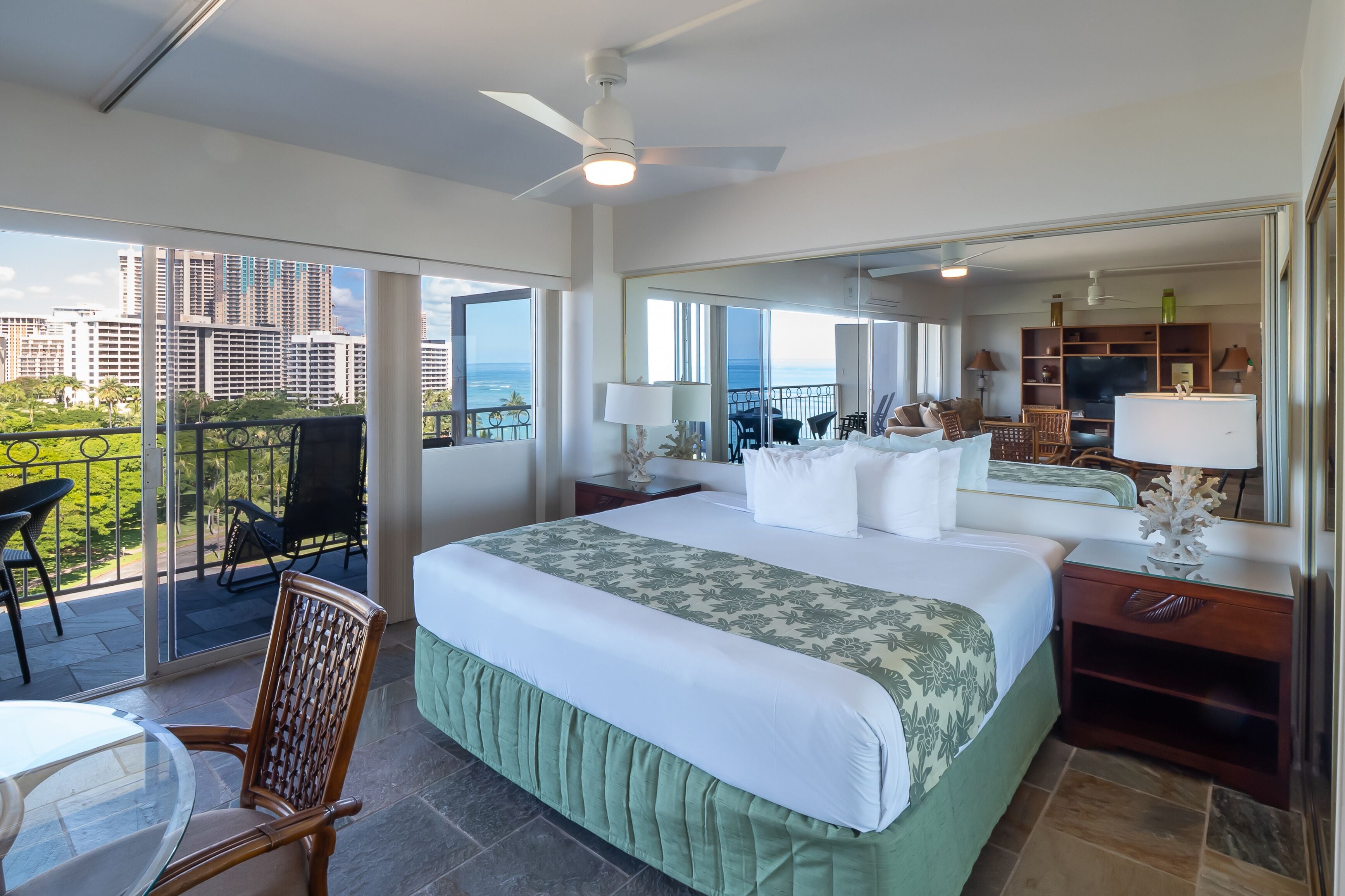 A hotel room with a balcony, a bed with a floral bedspread, a TV, and a seating area with a table and chairs.