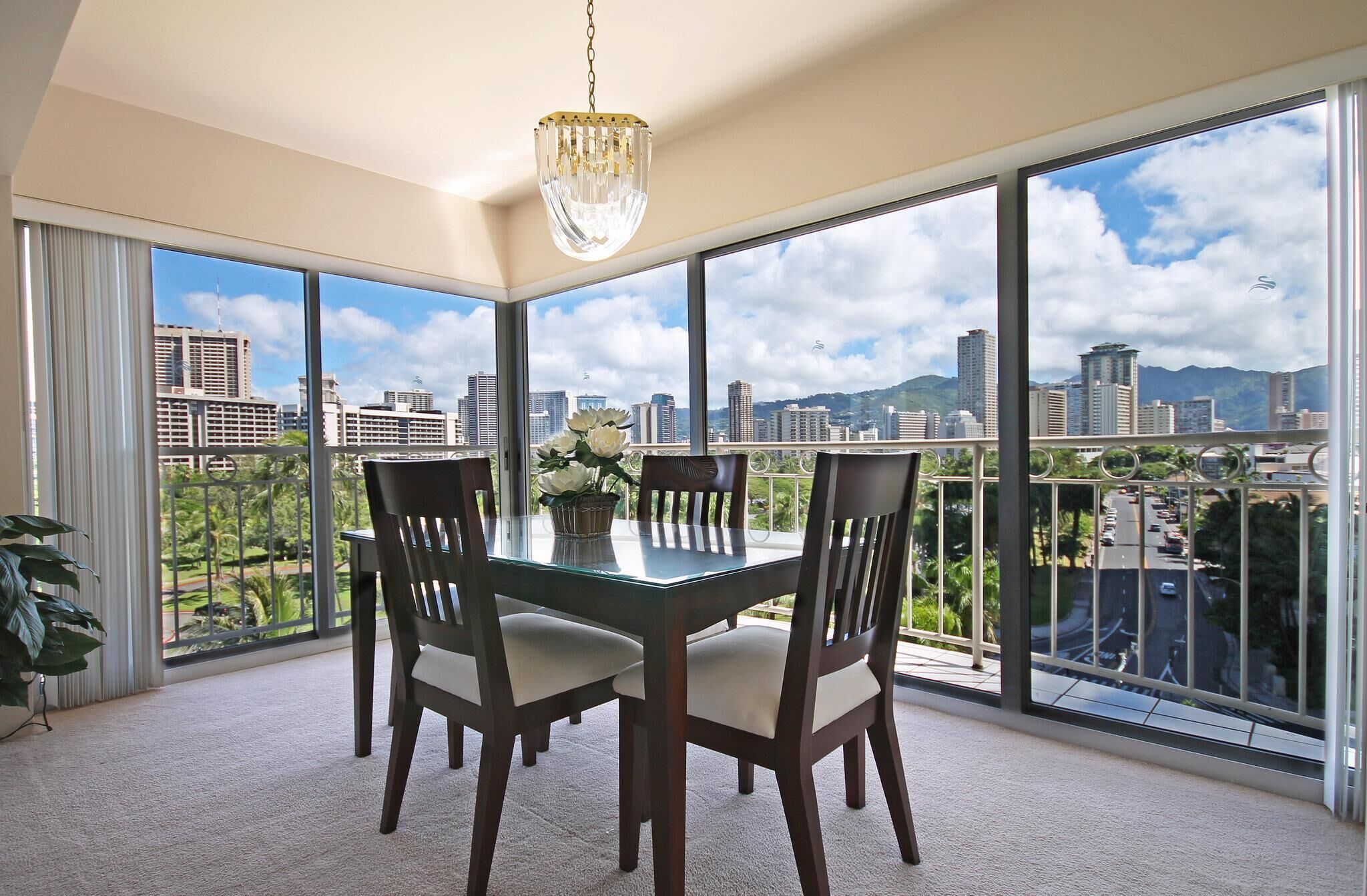 A dining area with a large table and four chairs, large windows with a city view, and a chandelier.