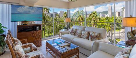 A spacious living room with a large TV, comfortable seating, and a balcony with a city view.