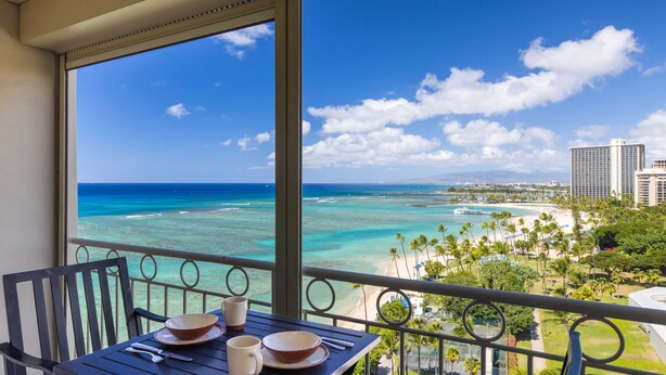 A balcony with a table set for two, overlooking a beach and ocean.