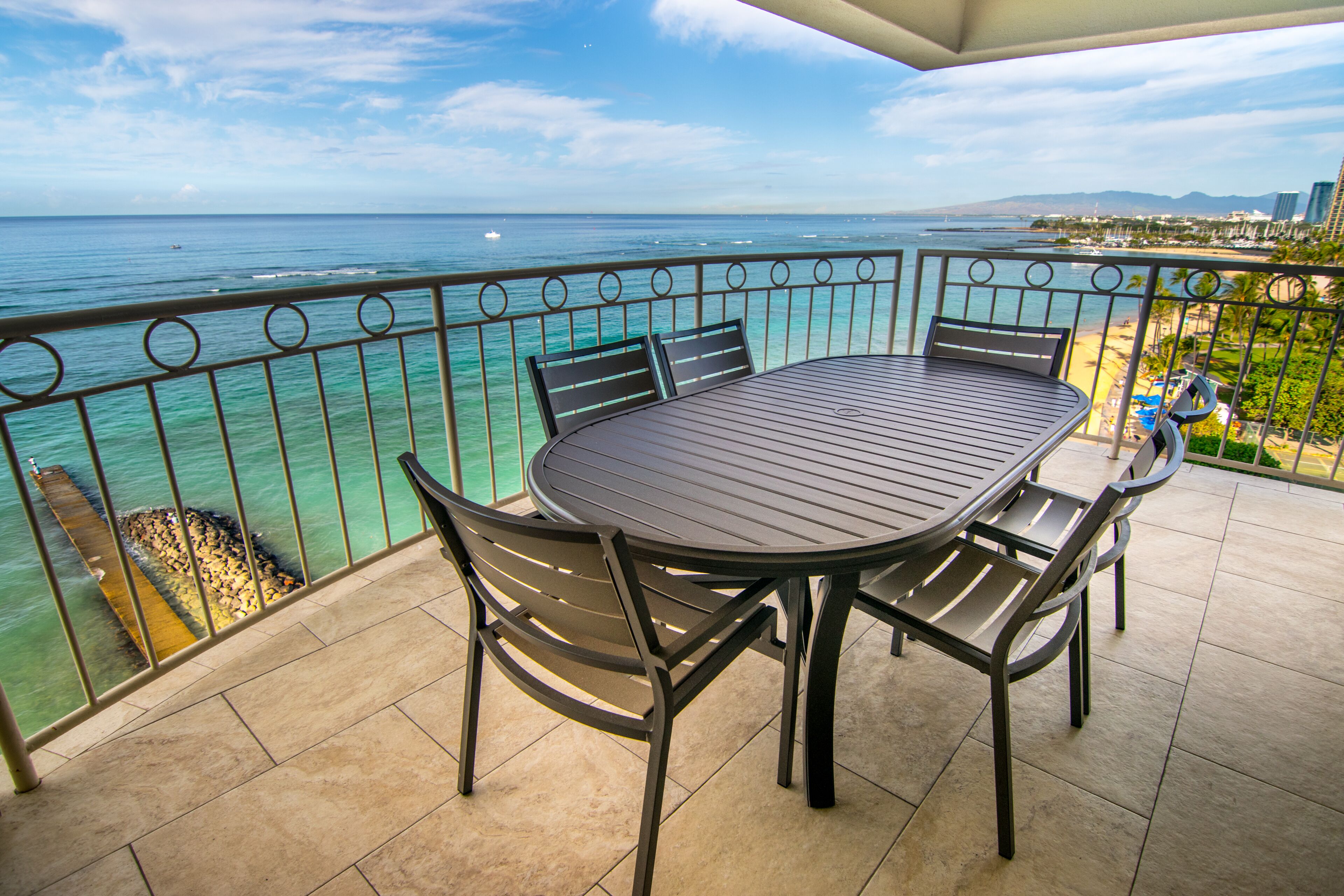 A balcony with a table and chairs, overlooking a beach and ocean.