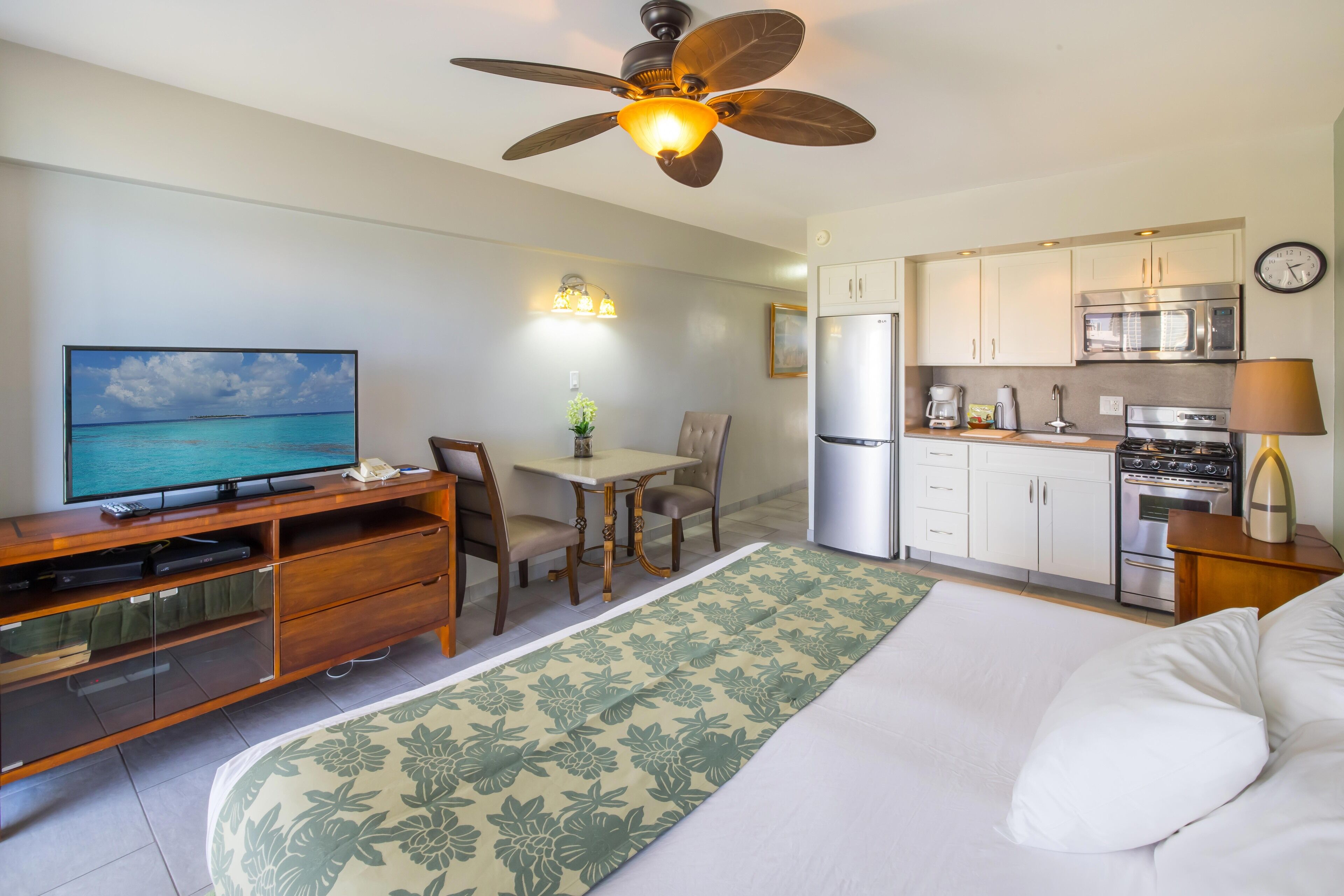 A compact hotel room with a bed, a desk with a television, a dining area, and a kitchenette.