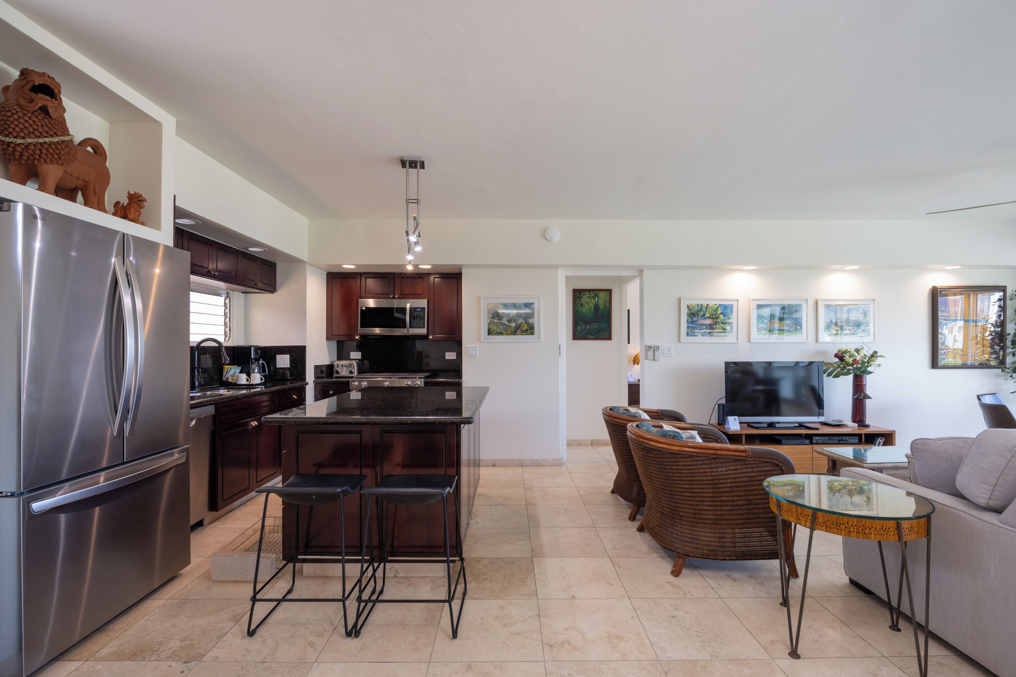 A modern kitchen with stainless steel appliances, a central island with bar stools, and a dining area with wicker furniture.