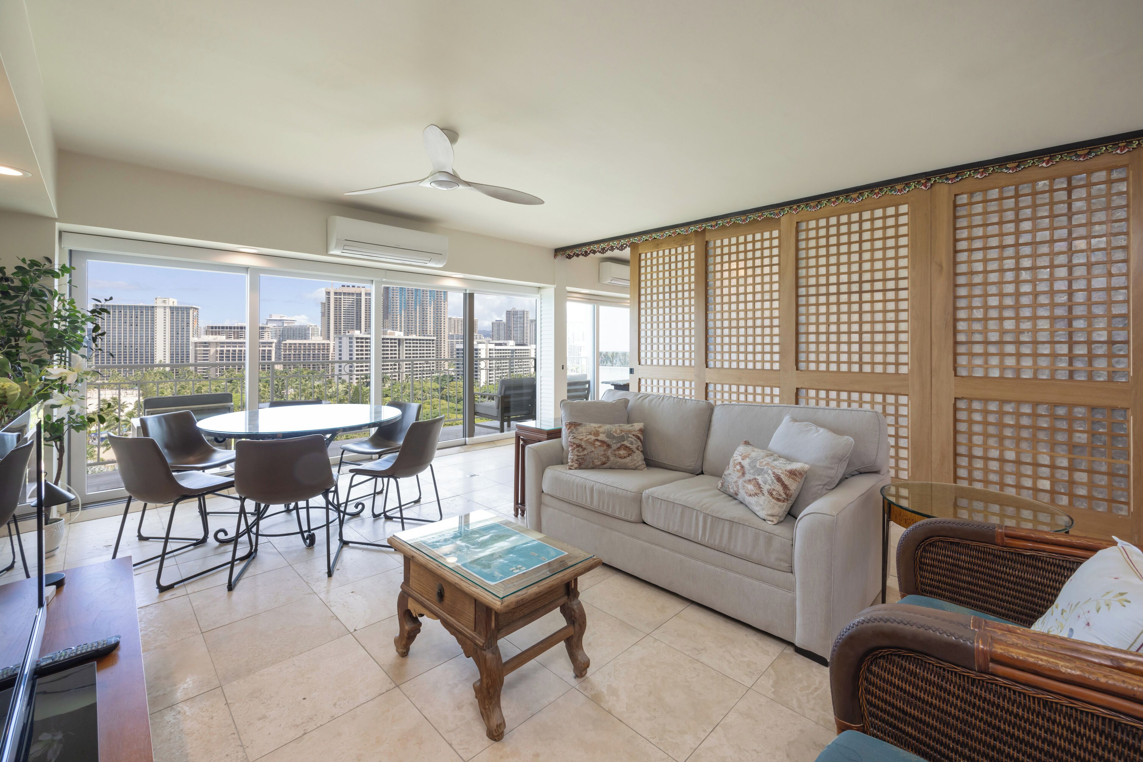 Un salón amplio con un gran ventanal, ventilador de techo, sofá, mesa de centro y mesa de comedor con sillas.