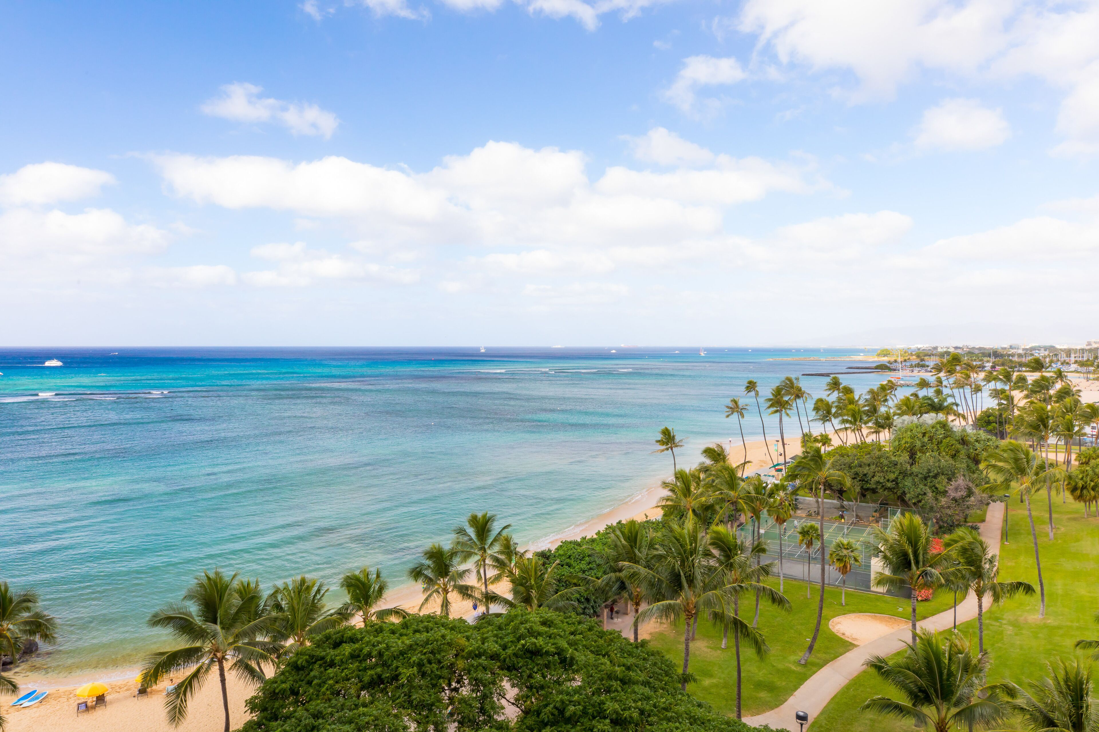 A beach view with palm trees, a tennis court, and a clear sky.