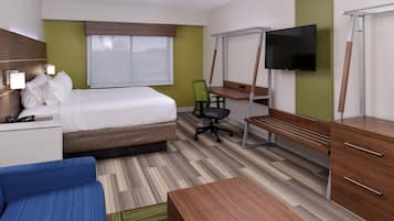 Quarto de hotel com cama, escrivaninha, cadeira, televisão e um pequeno sofá.
