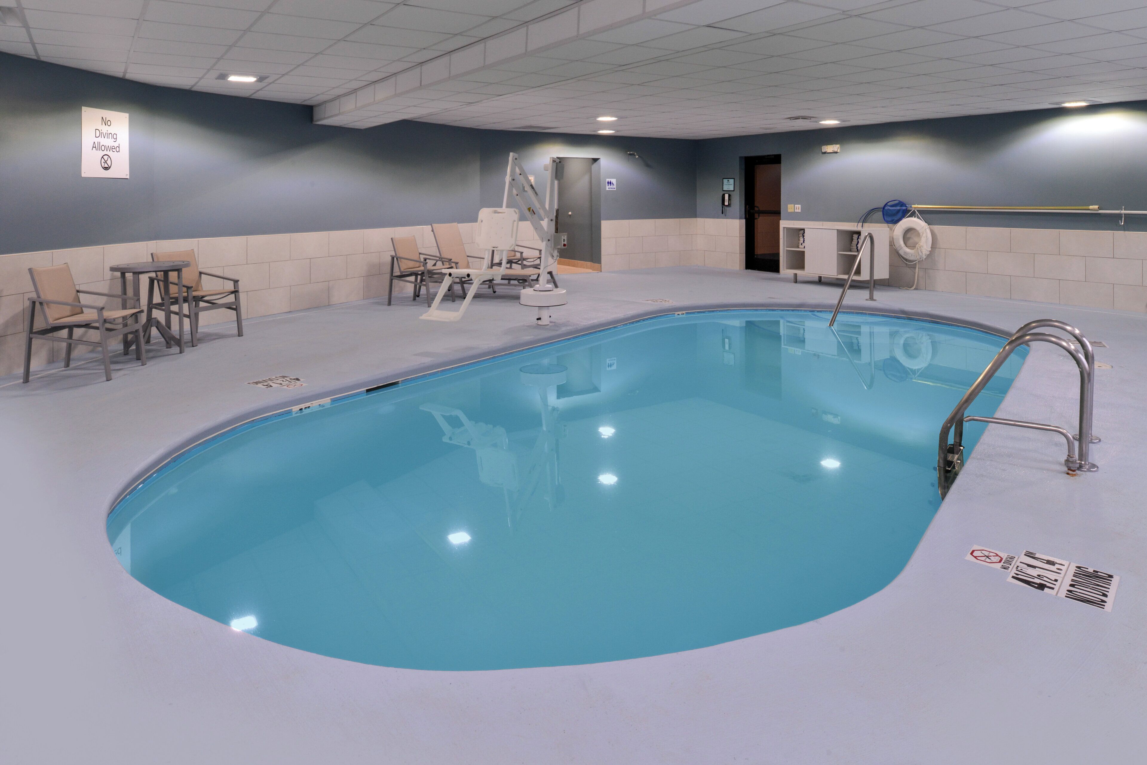 A swimming pool with a no diving sign, lounge chairs, and a changing room area.
