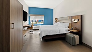 A modern bedroom with a bed, bedside table, and a desk with a chair. - Holiday Inn Express & Suites Raleigh NE - Medical Ctr Area by IHG (Raleigh)