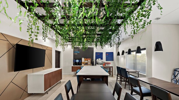 A modern meeting room with a long table, chairs, a TV, and a coffee station. - Holiday Inn Express & Suites Raleigh NE - Medical Ctr Area by IHG (Raleigh)