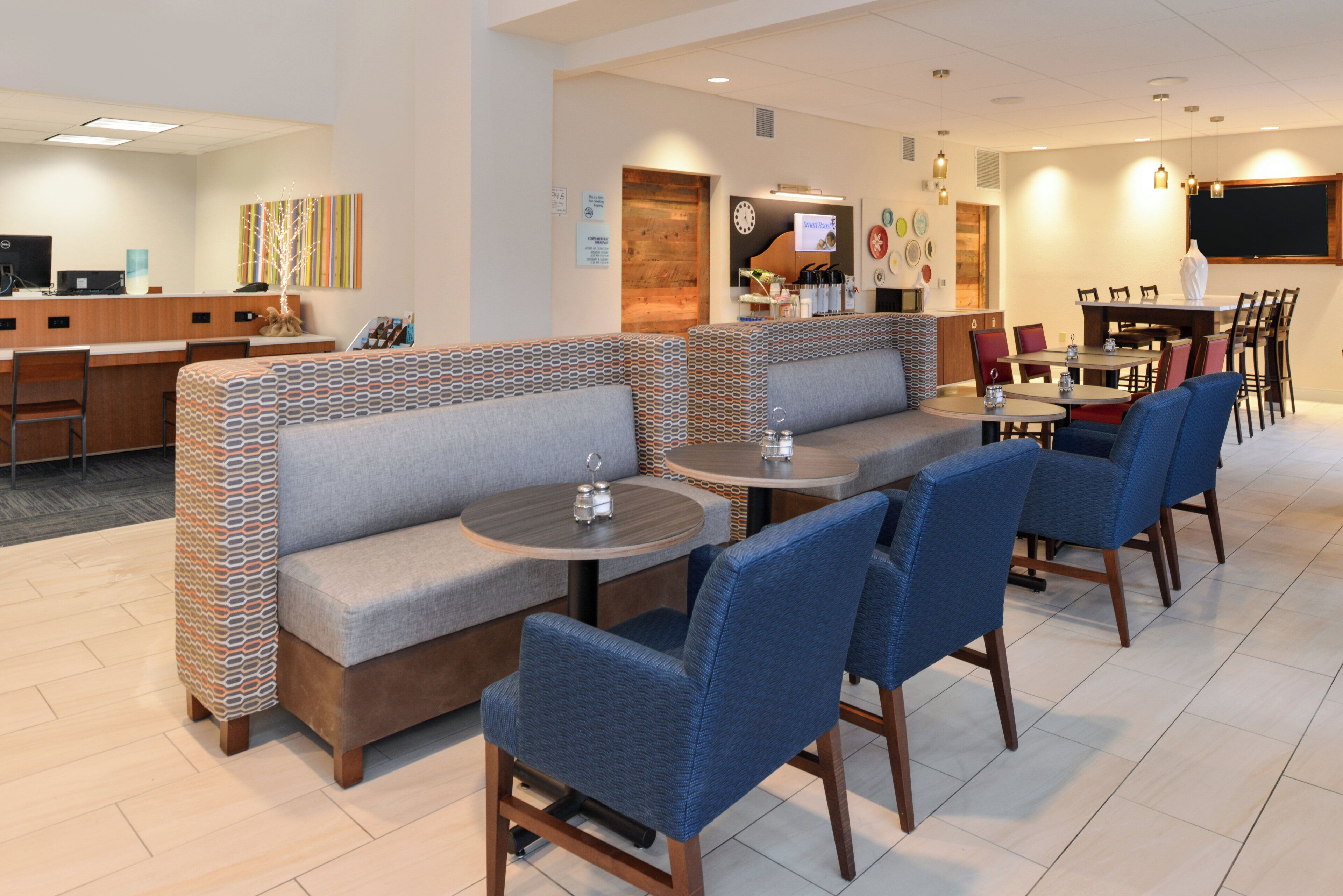 Un hall d’hôtel comprenant un comptoir d’accueil, un espace détente avec des canapés et des fauteuils, et un espace repas avec des tables et des chaises.