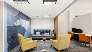 A modern hotel room with a sofa, two yellow armchairs, a small round table with a fruit bowl, a desk with a computer, and a map mural on the wall. - Holiday Inn Express & Suites Raleigh NE - Medical Ctr Area by IHG (Raleigh)