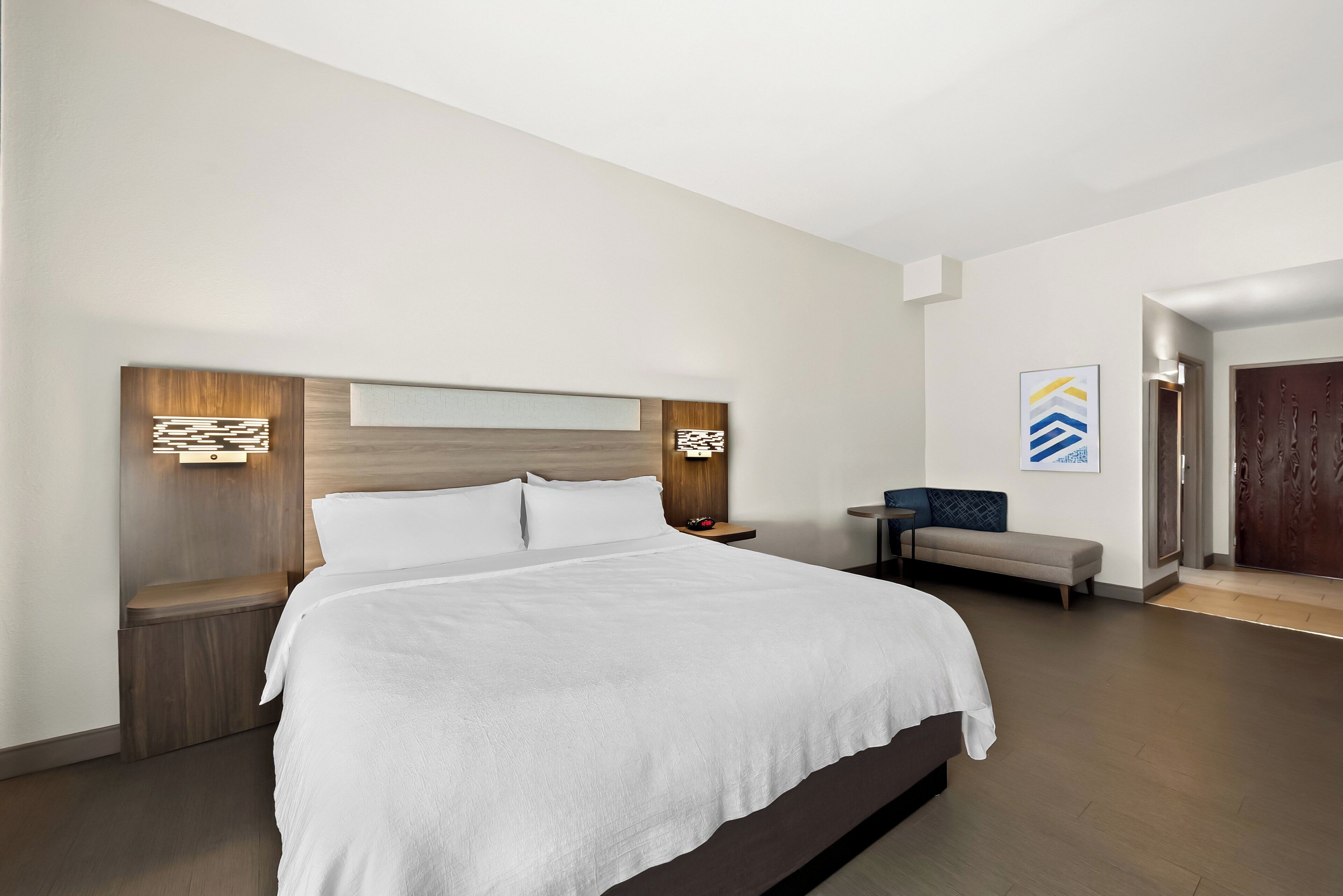 Une chambre d’hôtel moderne avec un grand lit, des tables de chevet, un banc et une porte.