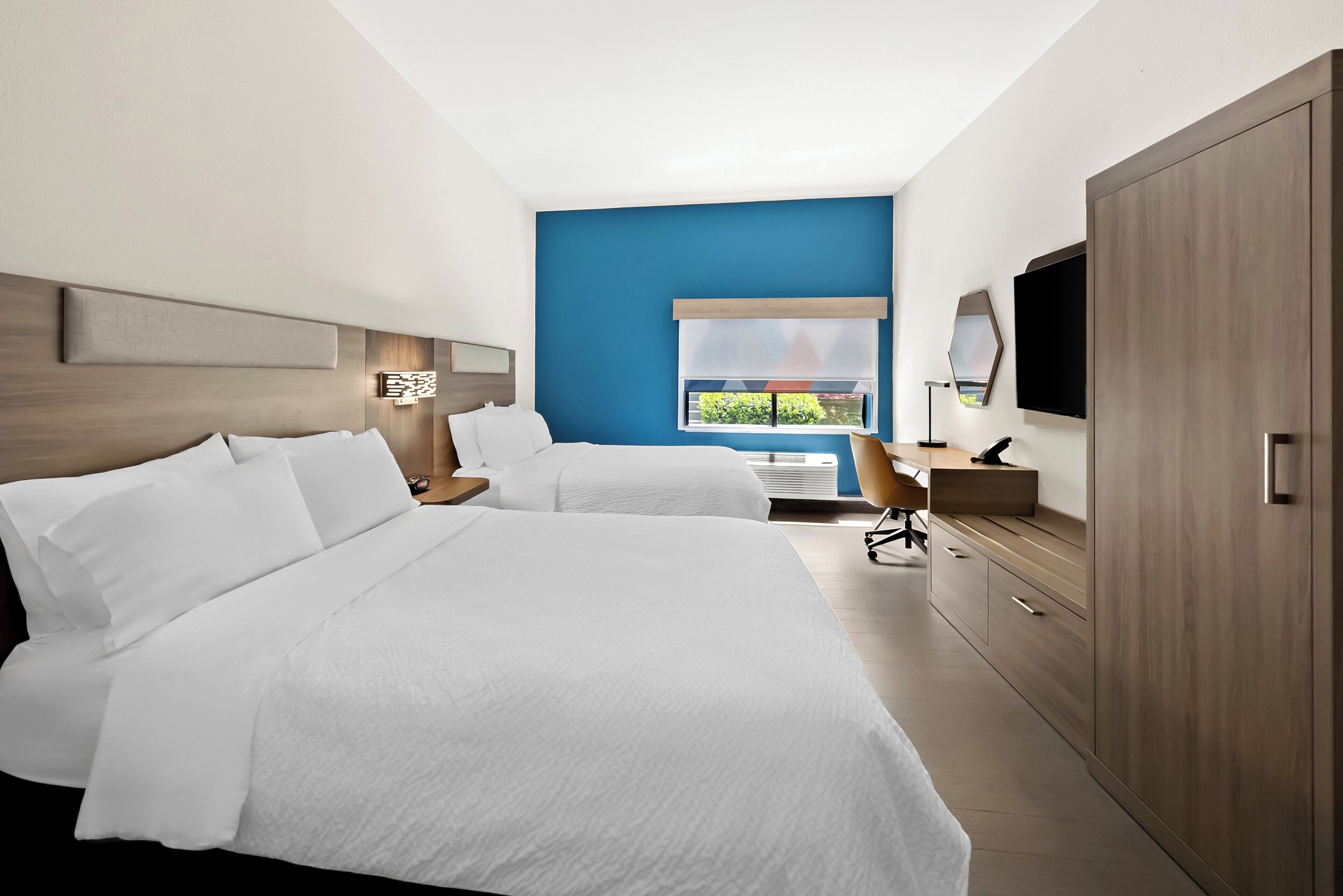 Une chambre d’hôtel avec deux lits, un bureau, une chaise, une télévision et une armoire.