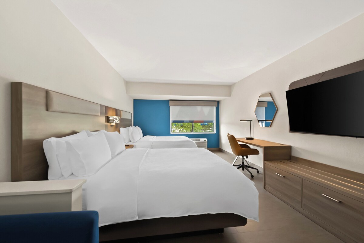 A hotel room with two beds, a desk, a chair, a TV, and a window with a view.
