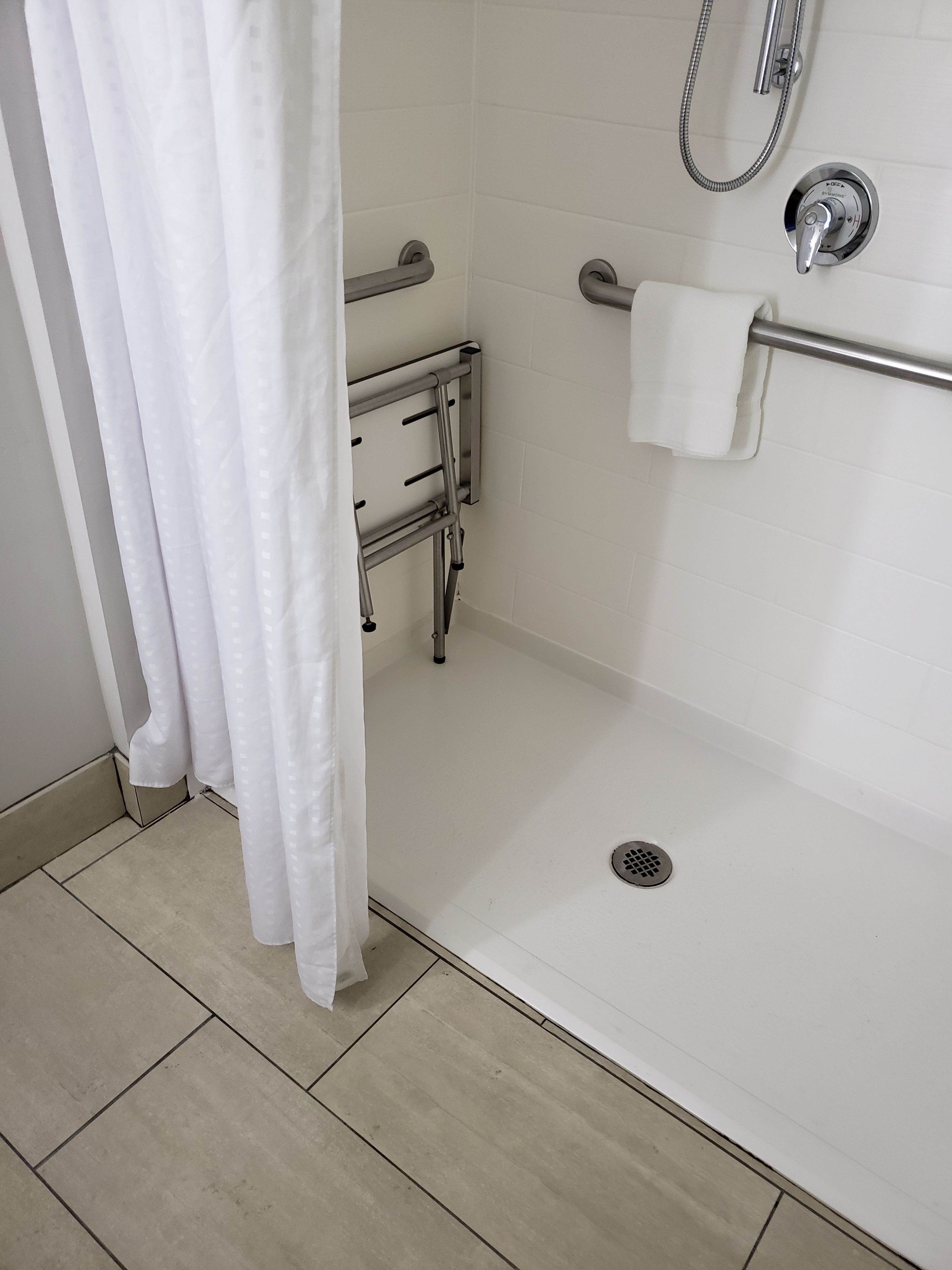 A modern bathroom with a shower, grab bars, a towel rack, and a toilet.