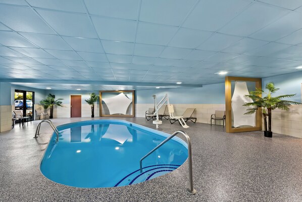 An indoor swimming pool with a blue tiled floor, a clear pool, and a few lounge chairs and potted plants around. - Holiday Inn Express & Suites Raleigh NE - Medical Ctr Area by IHG (Raleigh)