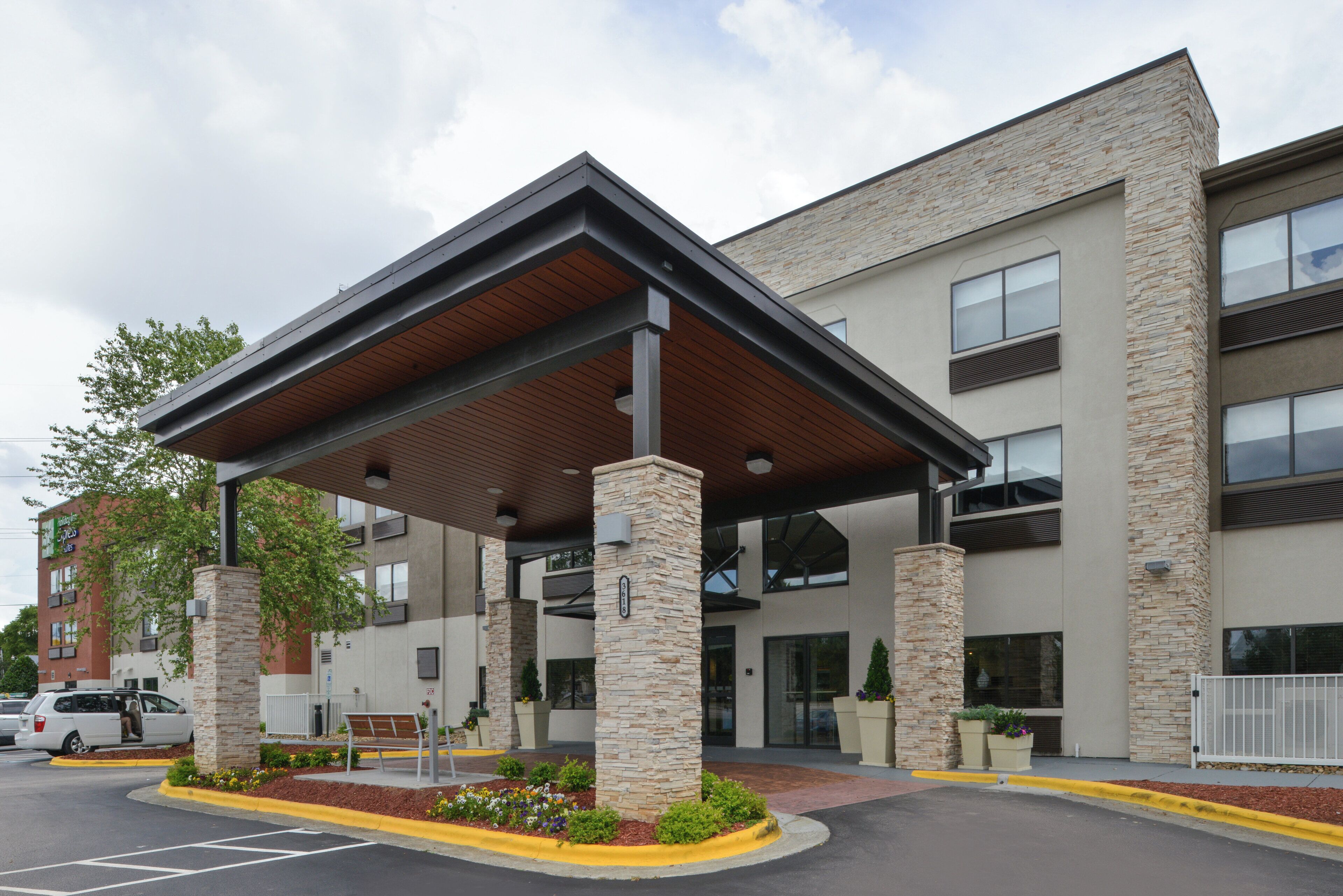 A hotel entrance with a covered patio, stone pillars, and a parking lot.