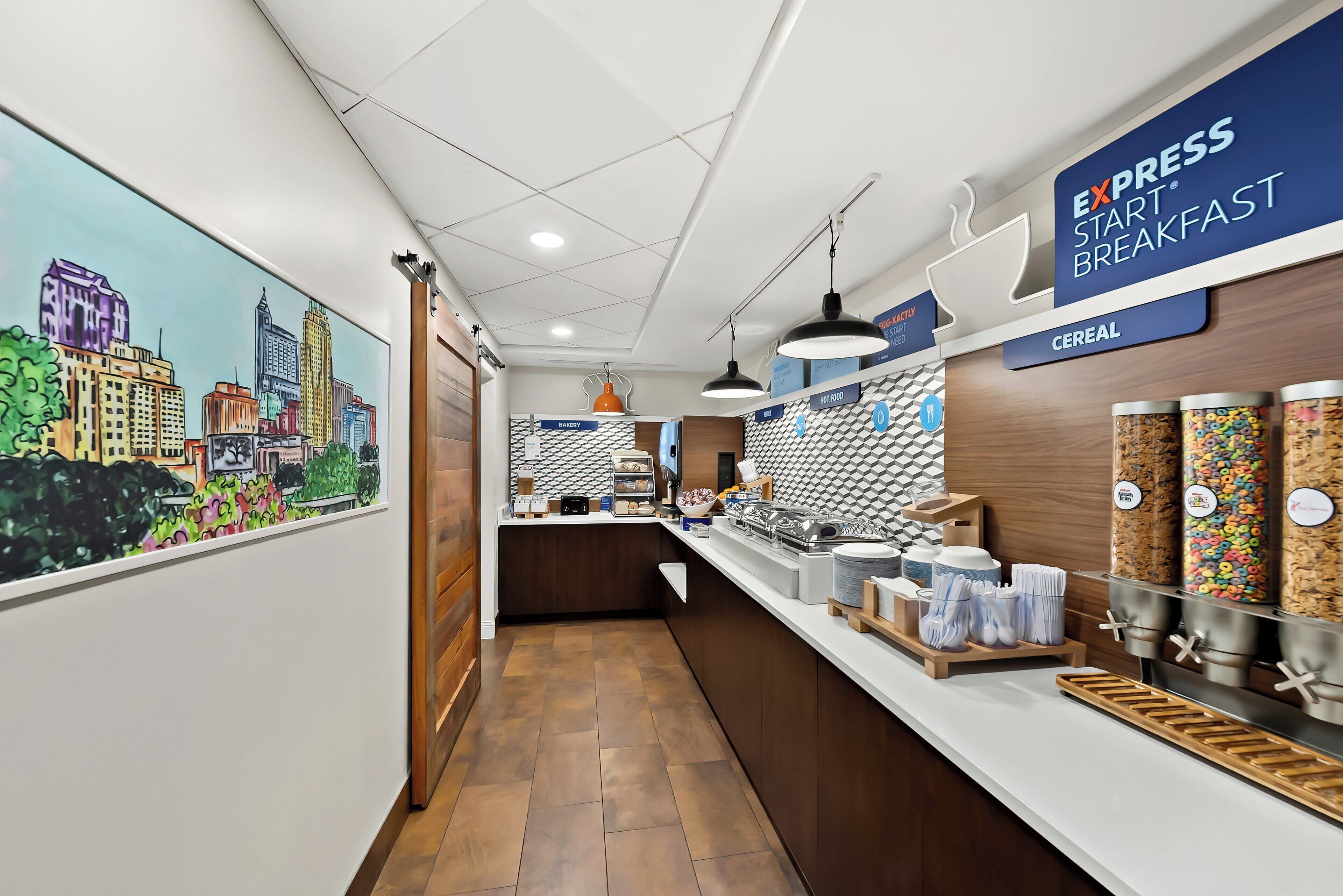 A modern breakfast area with a cityscape mural, a sign for 'EXPRESS START BREAKFAST', and various food dispensers.