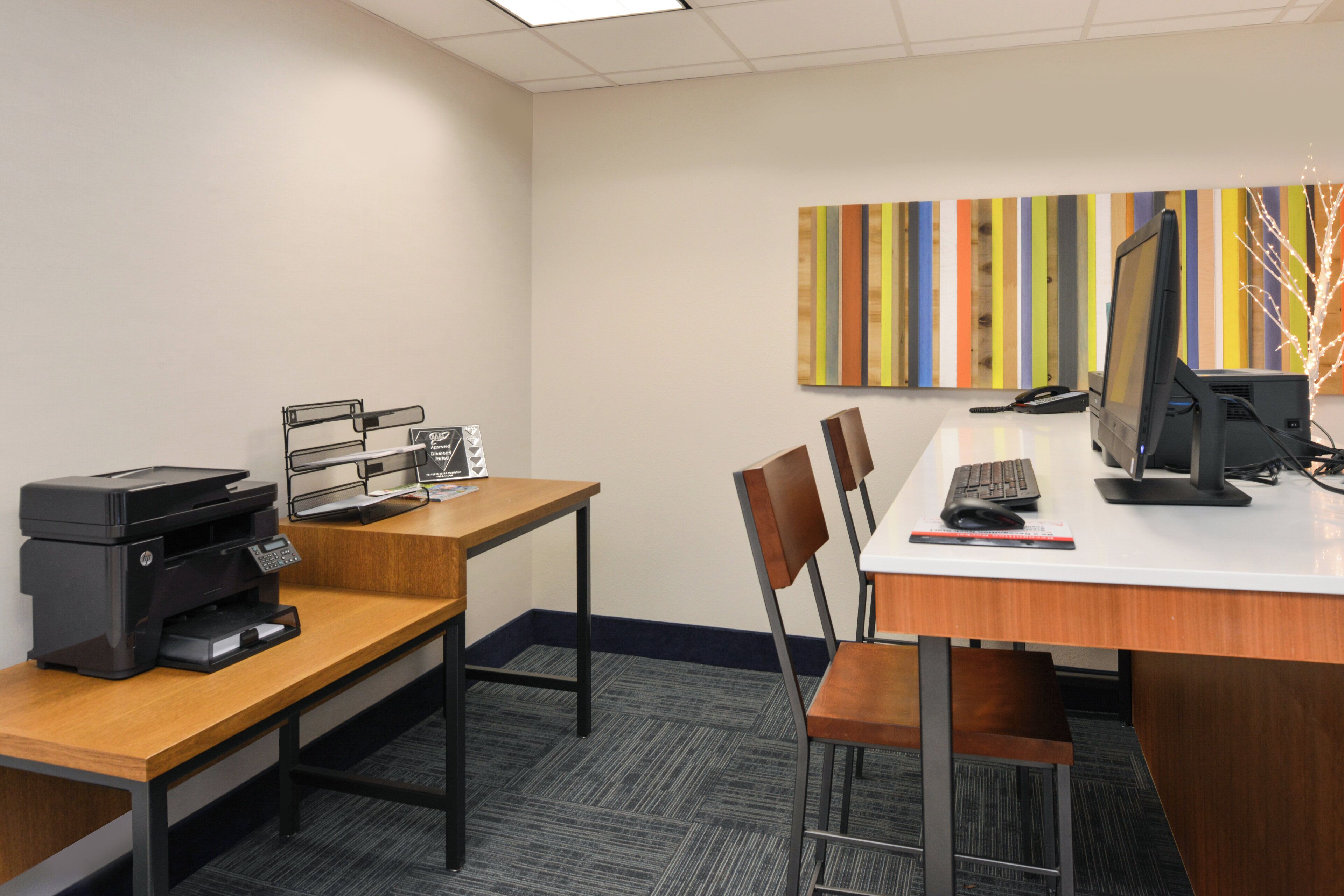 Un espace de bureau moderne comprenant un bureau, une imprimante, un ordinateur et des chaises.
