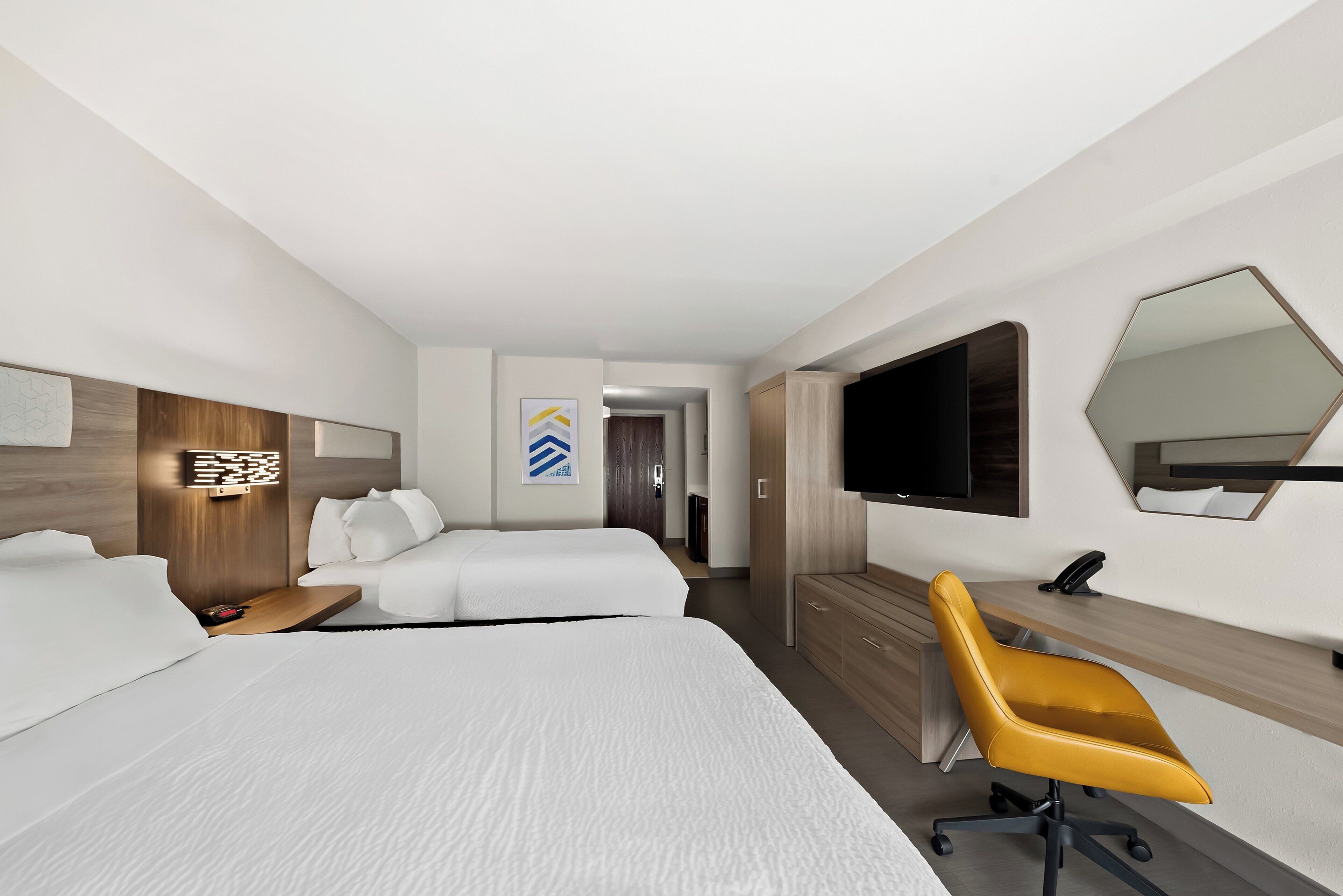 A modern hotel room with two beds, a desk, a chair, a TV, and a mirror.